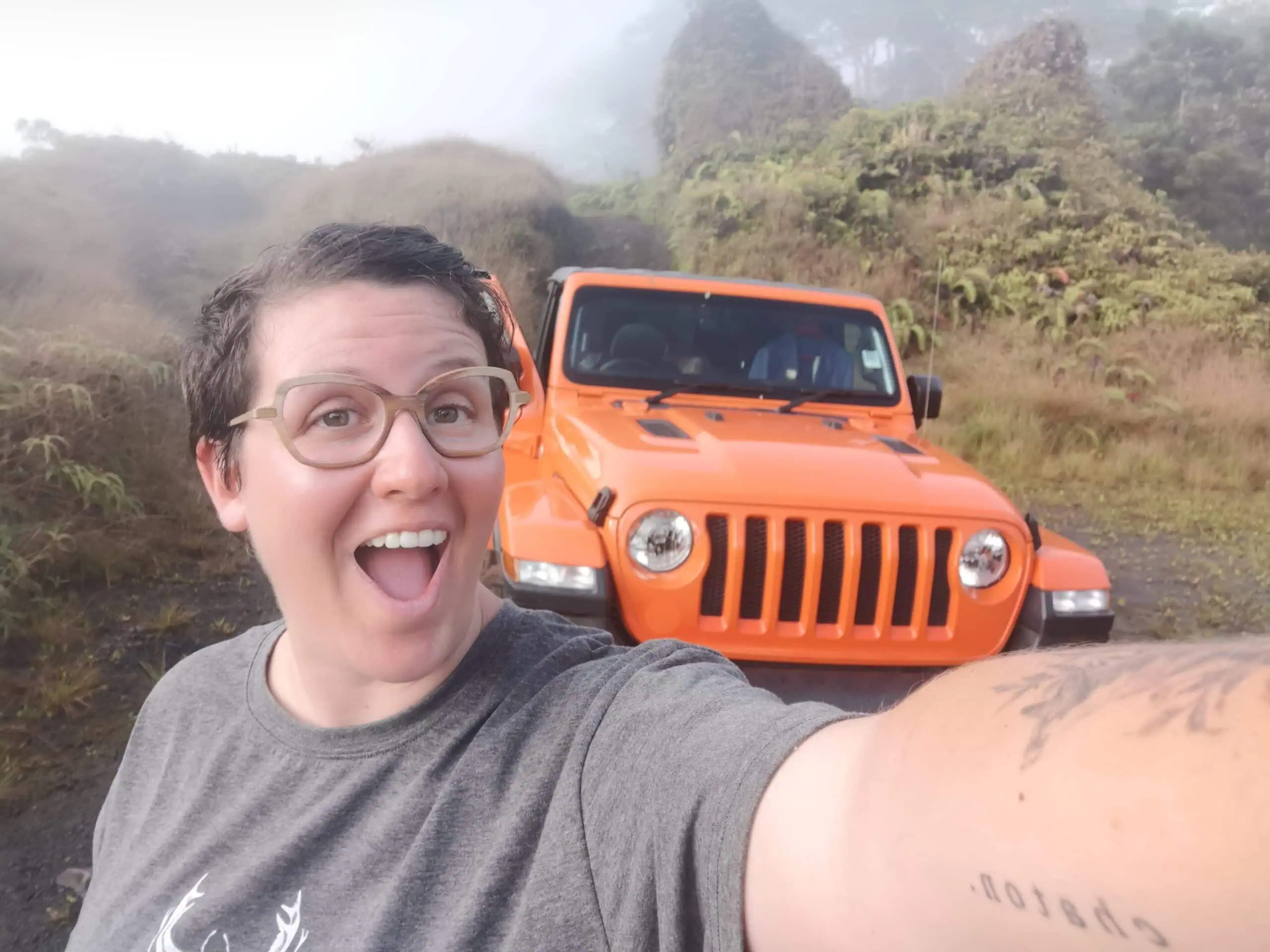 Elopement couple with a vibrant orange Jeep in lush tropical landscape.