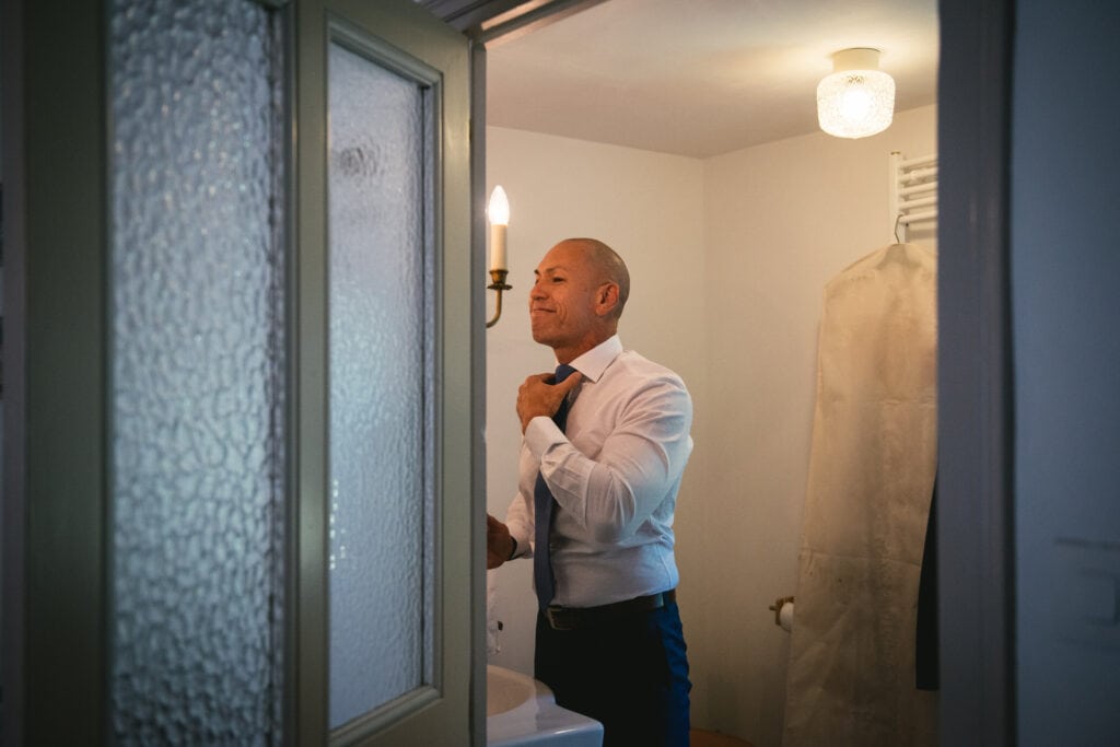 Groom putting his tie in front of the bathroom mirror before his elopement ceremony