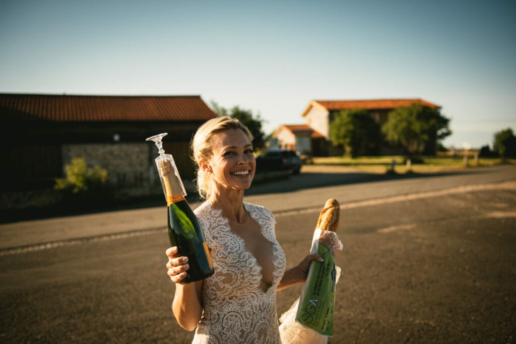 Bride holding some glasses and a bottle of champagne at sunset