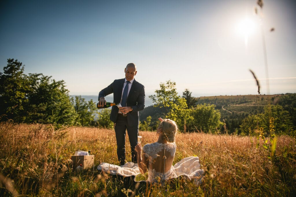 Groom pouring a glass of champagne in a field at sunset after their elopement in Central France