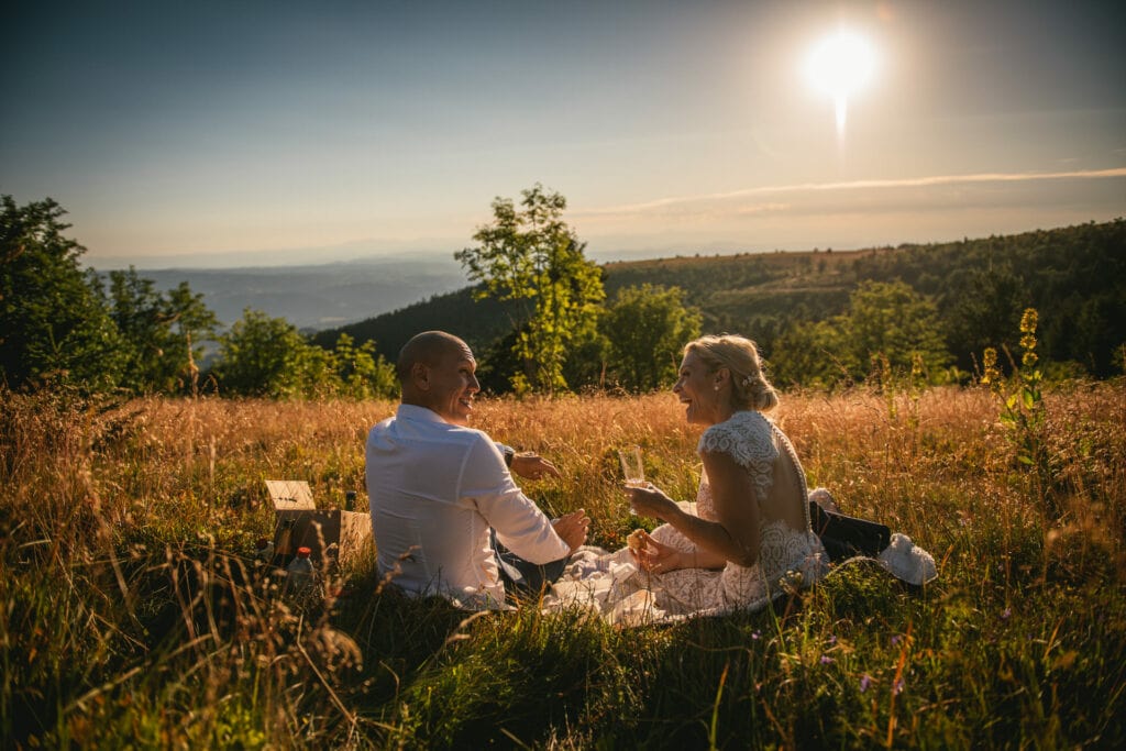 Bride and groom laughing while they eat a picnic at sunset after their elopement in Central France