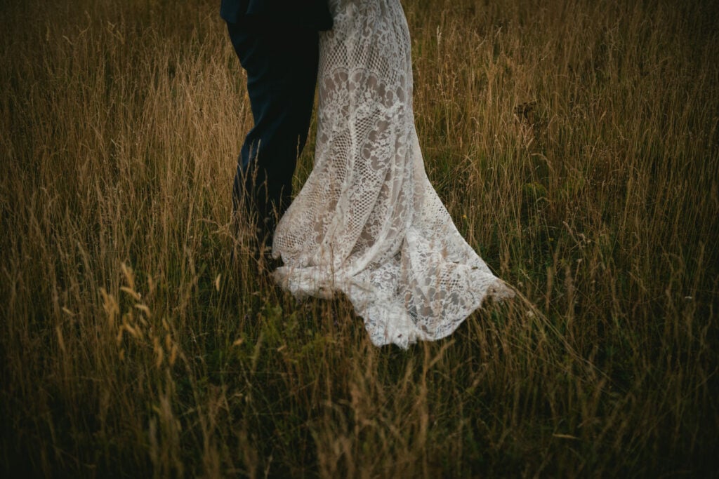 Detail shot of a lace wedding dress and a blue suit in a field
