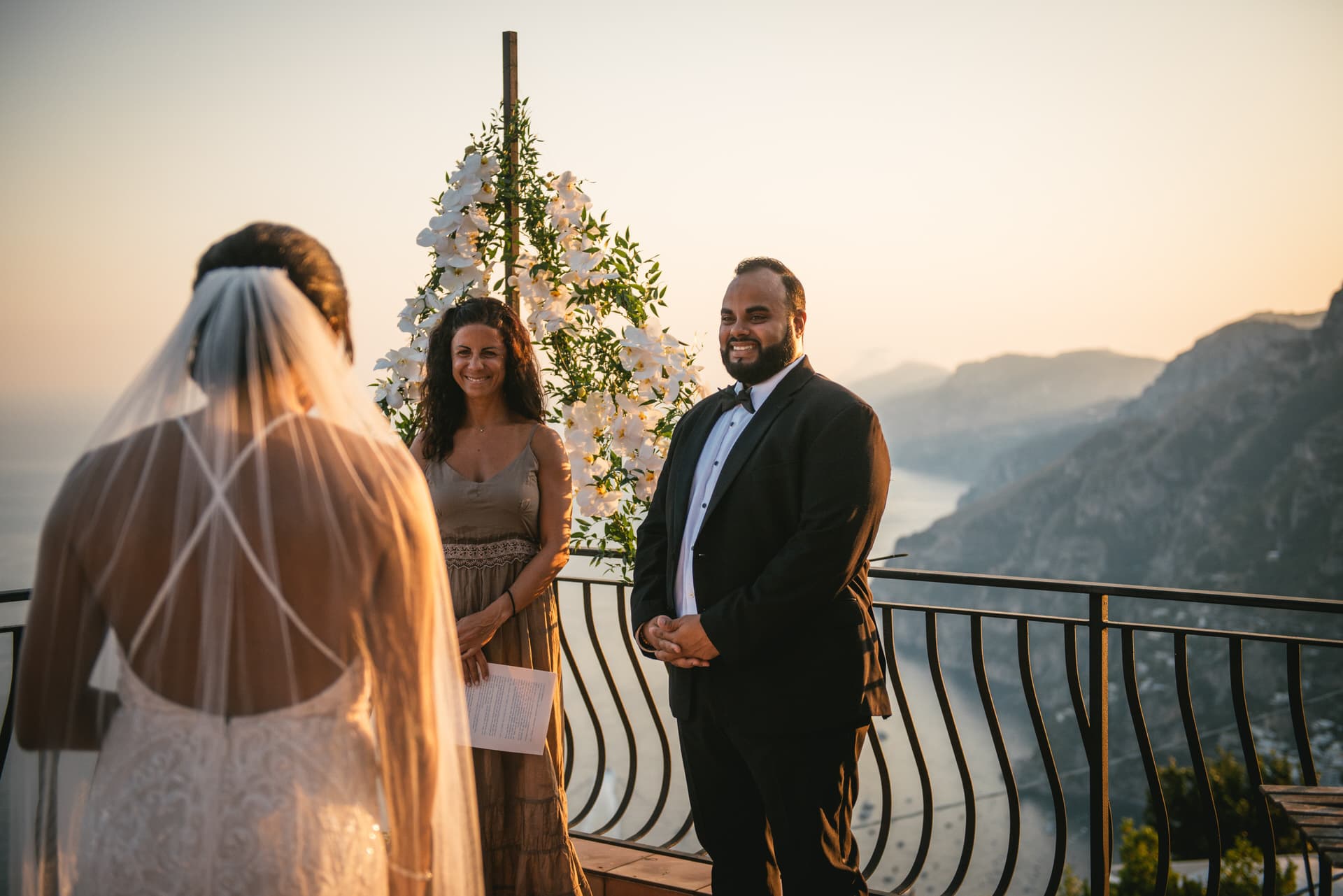 Bride walking down the aisle to her future husband with the town of Positano in the background at sunset