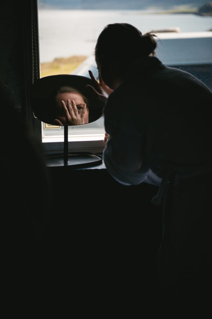 Bride putting makeup on by the window of her cottage in Iceland