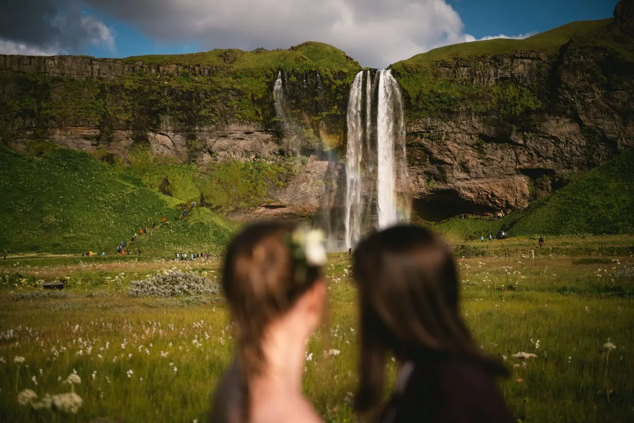 Same-sex couple posing in front of Seljalandsfoss during their elopement ceremony in Iceland
