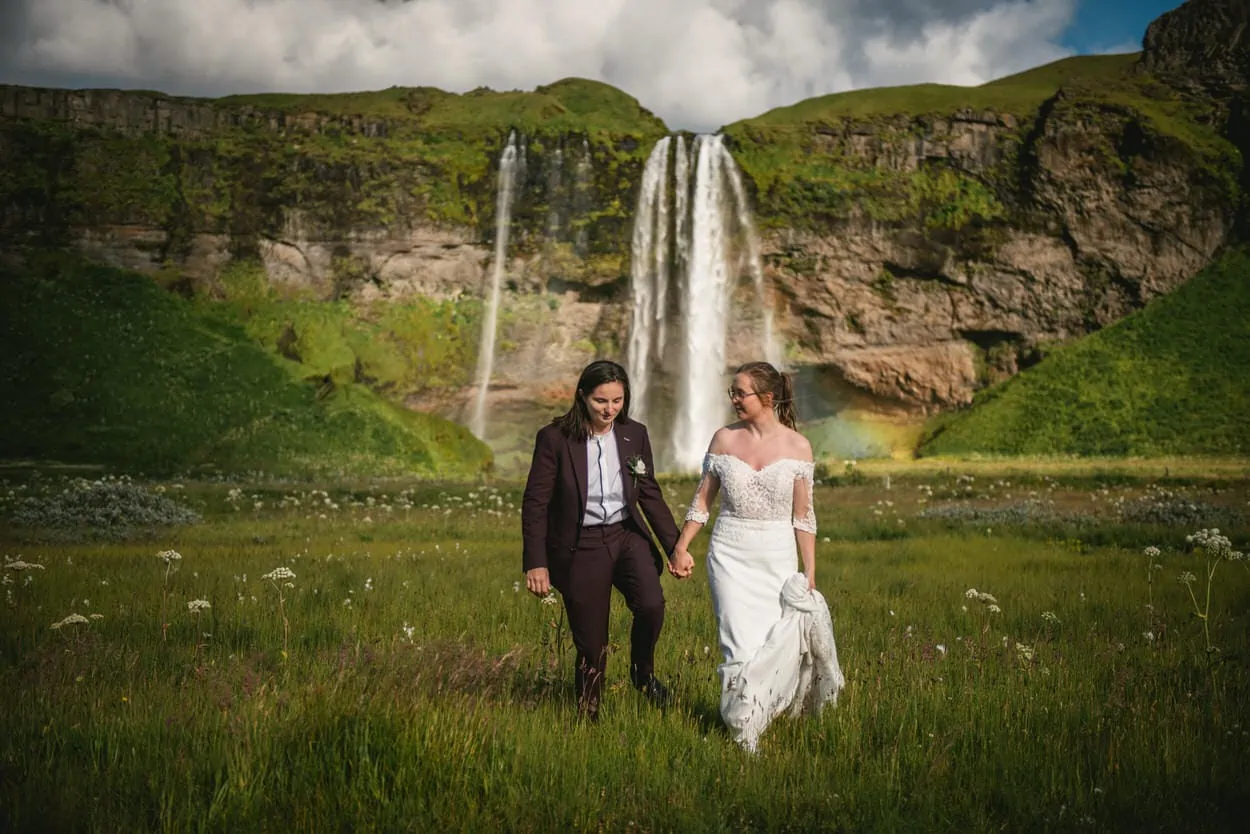 Same-sex couple posing in front of Seljalandsfoss during their elopement ceremony in Iceland