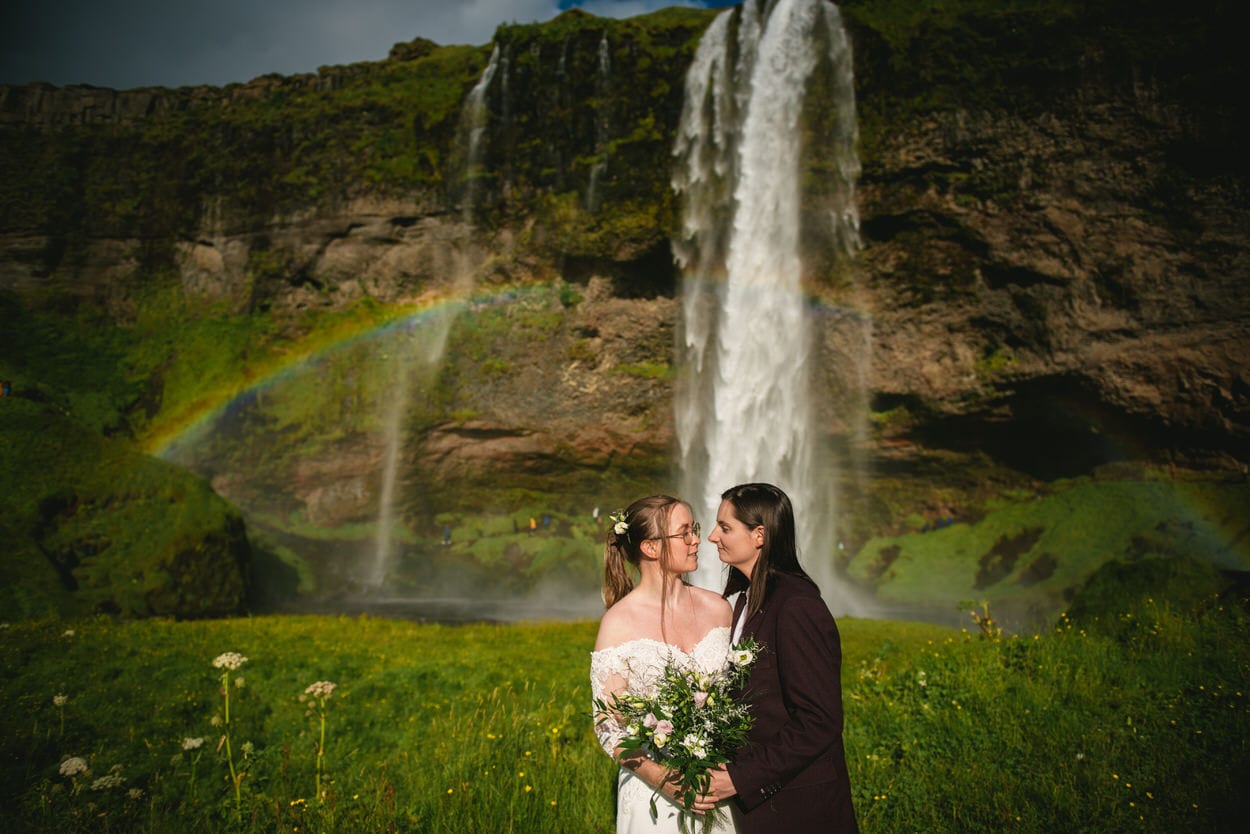 Same-sex couple posing in front of Seljalandsfoss during their elopement ceremony in Iceland