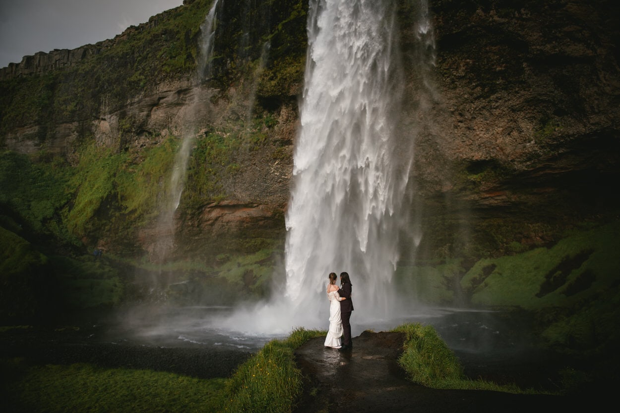 Same-sex couple posing in front of Seljalandsfoss during their elopement ceremony in Iceland