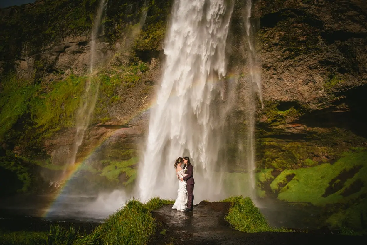 Same-sex couple posing in front of Seljalandsfoss during their elopement ceremony in Iceland