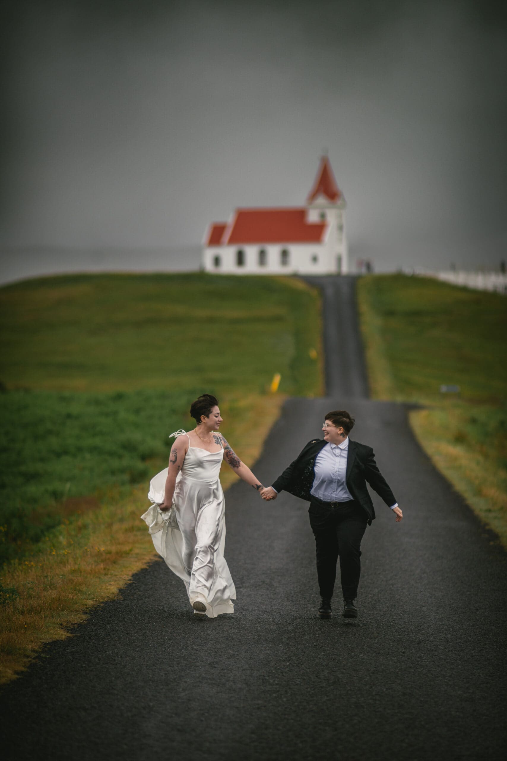 Two brides running away from a red and white icelandic church on their elopement day