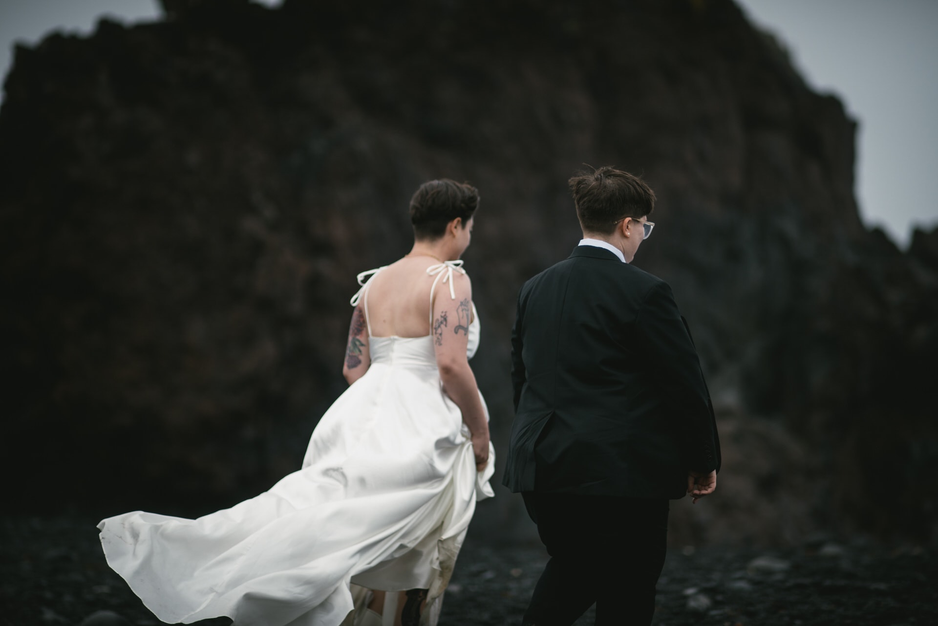 Two brides walking on a black beach in the summer icelandic wind