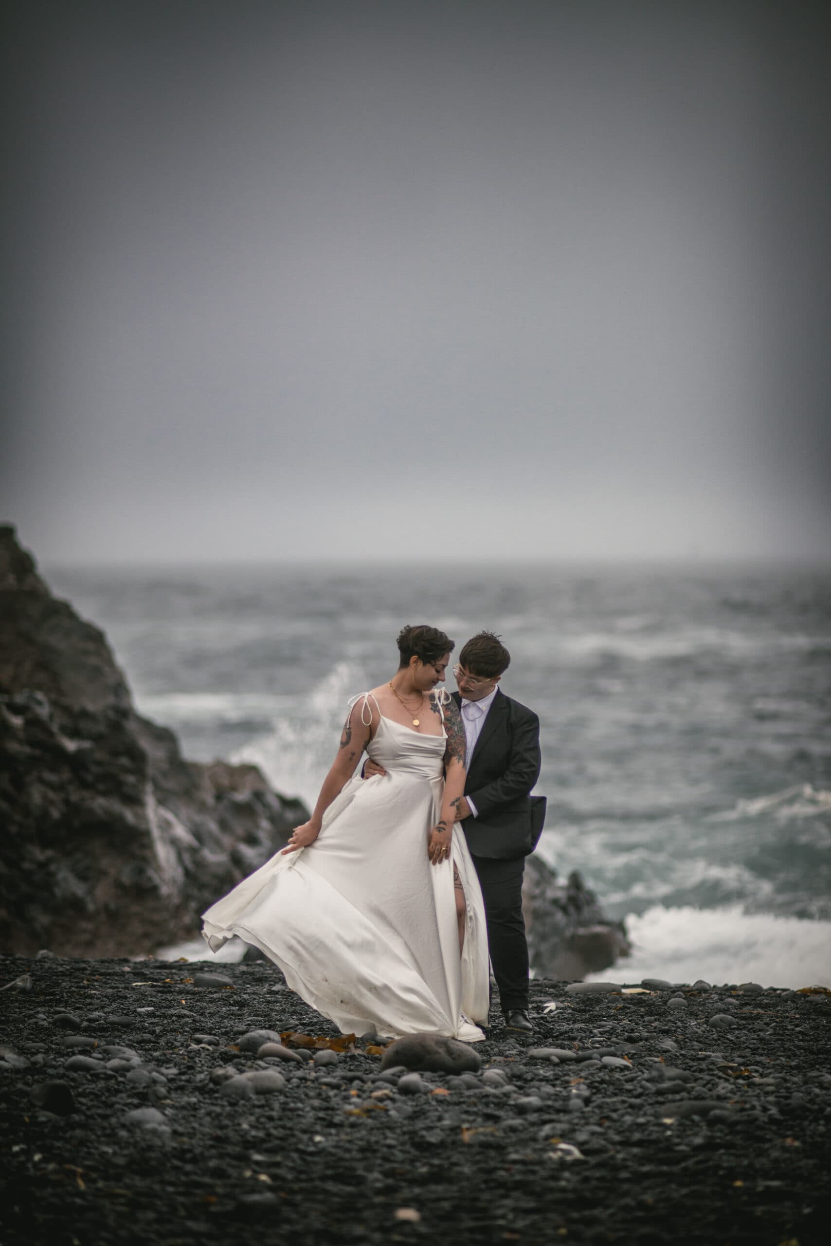 Two brides posing in front of the ocean with waves in the background on their elopement day in Iceland