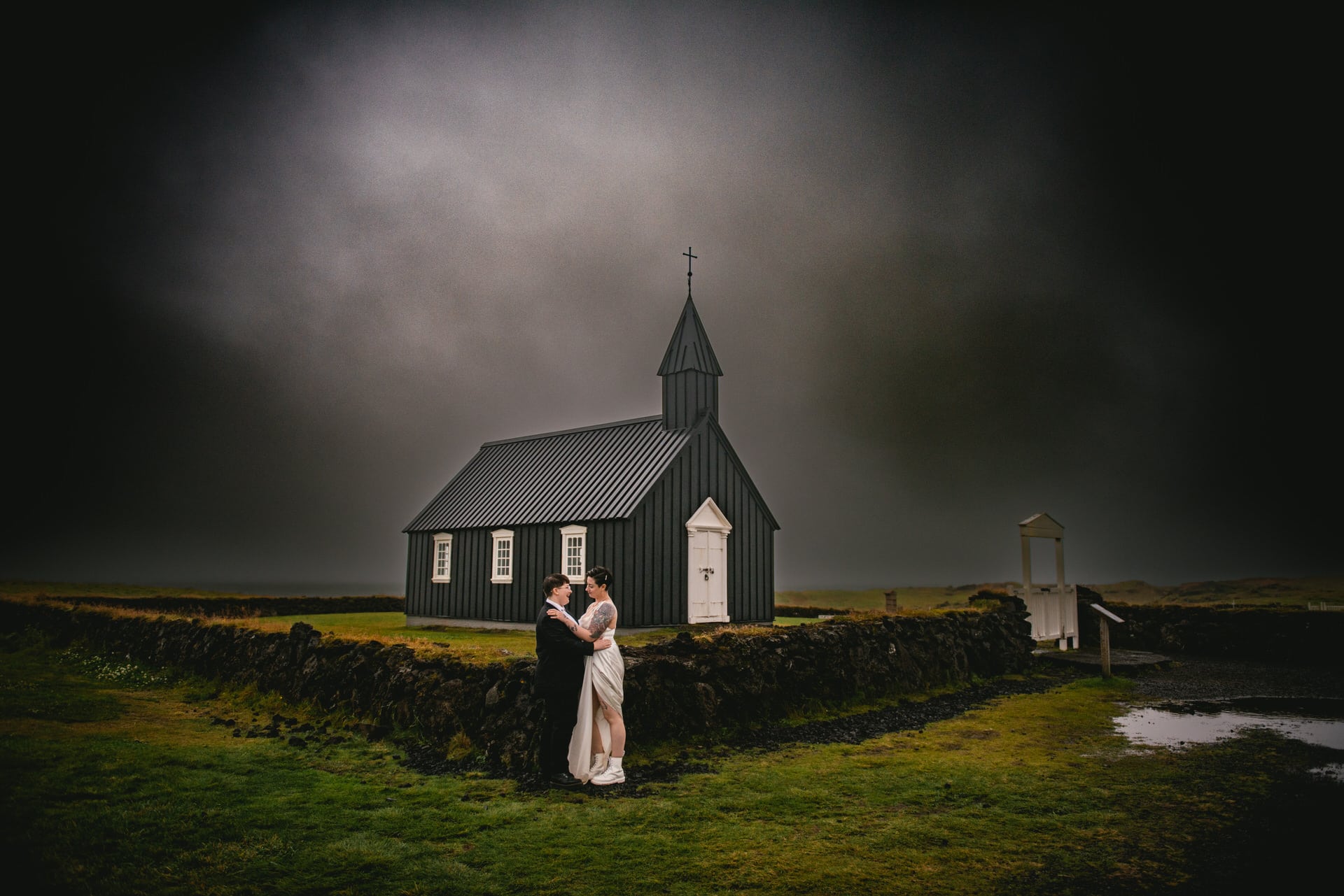 Same-sex couple posing in front of the Budhir black icelandic church on their elopement day in Iceland