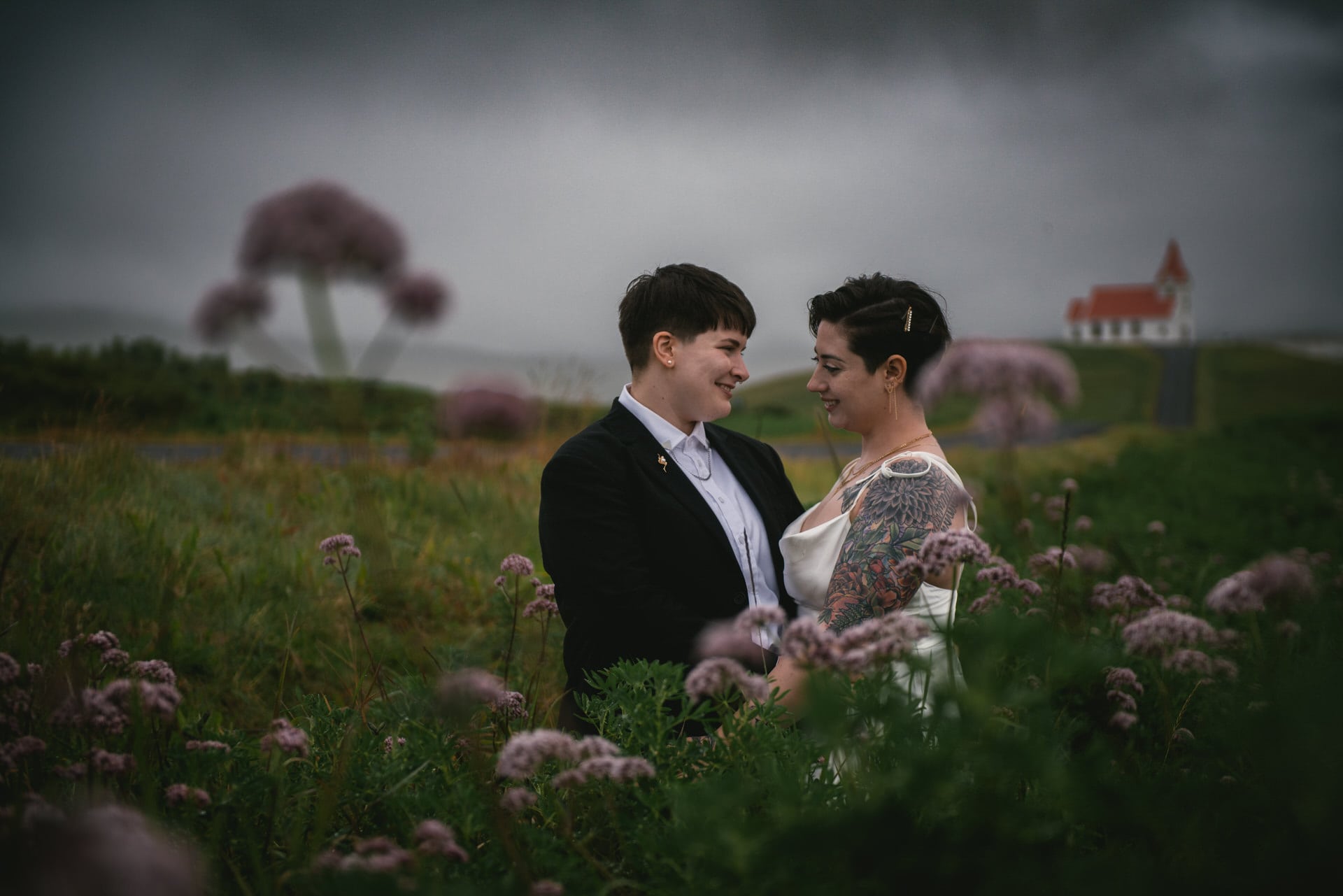 Same-sex couple looking at each other in a field of flowers on a rainy day