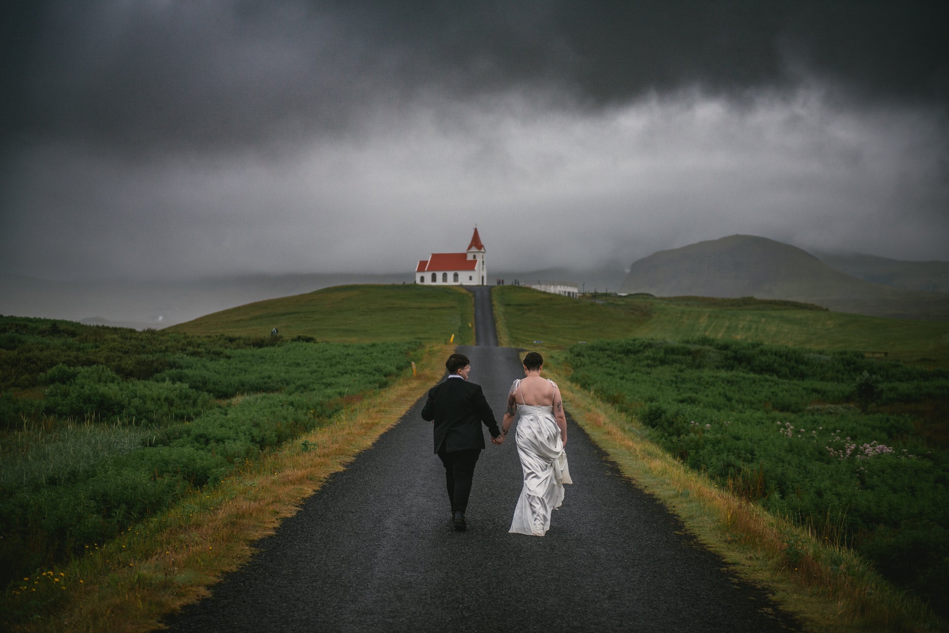 Same-sex couple walking towards a white and red church on their elopement day in Iceland