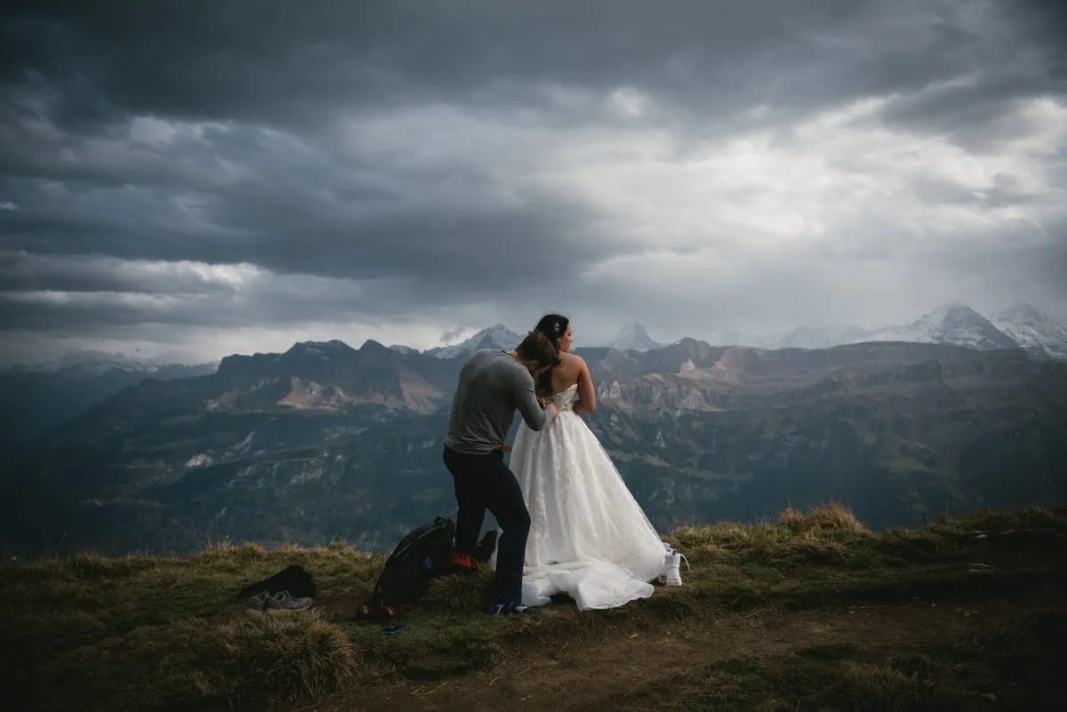 Couple on their elopement day in the Interlaken region of Switzerland - couple putting their wedding clothes on top of a mountain