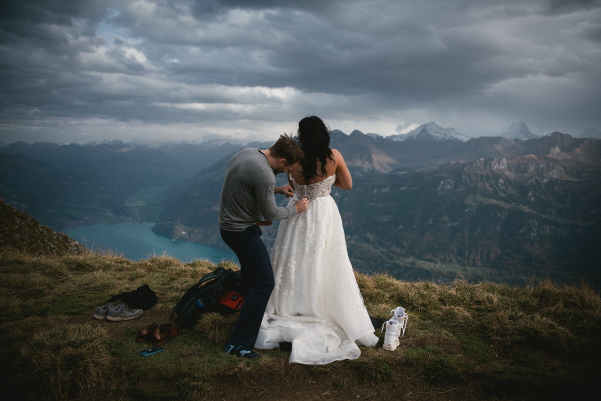 Couple on their elopement day in the Interlaken region of Switzerland - couple putting their wedding clothes on top of a mountain
