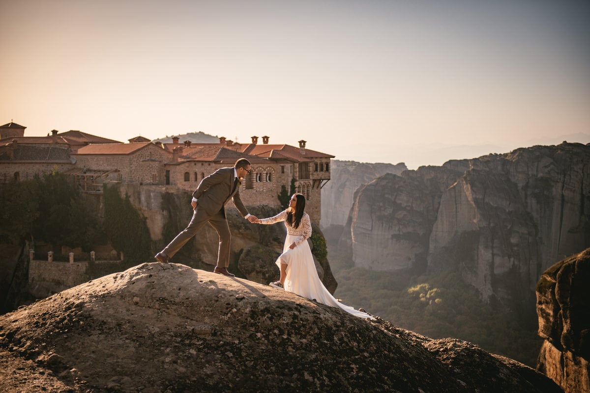 Couple holding hands with a monastery in the background on their day after photoshoot in the Meteora in Greece