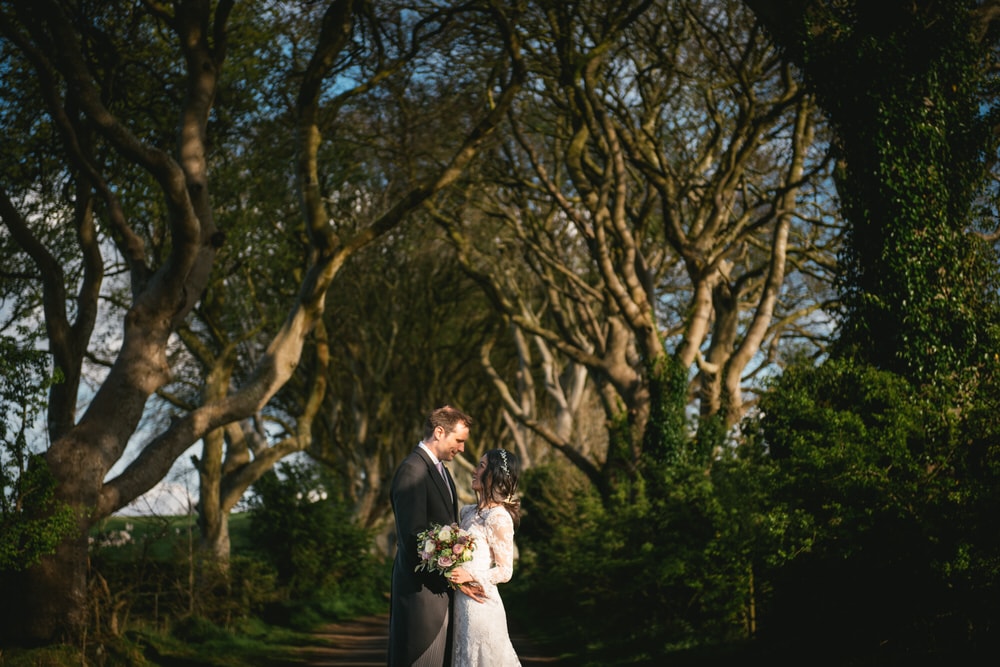 The bride and groom sharing a tender moment under the archway of trees in the forest during their Northern Ireland elopement.