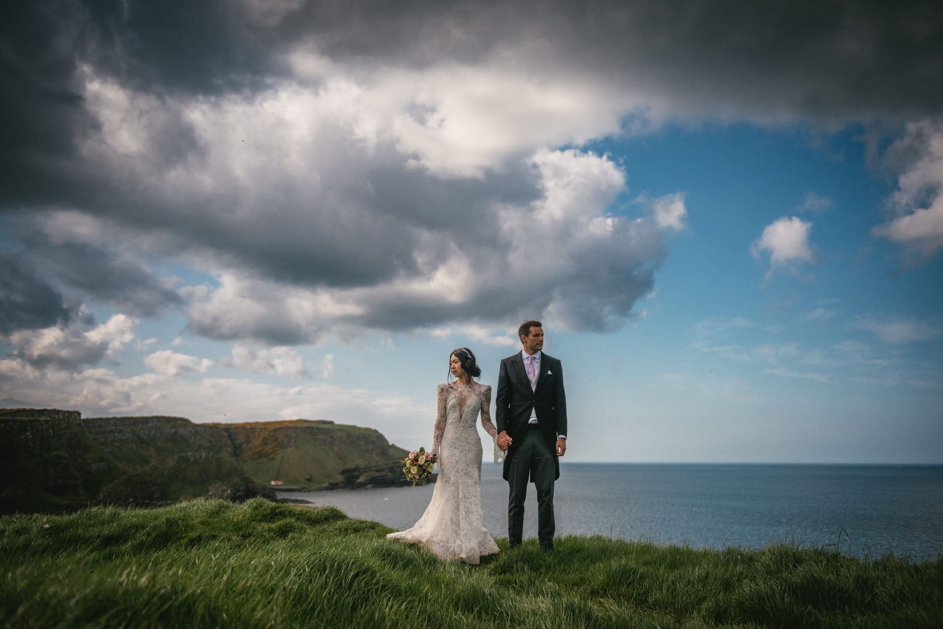 The couple walking hand in hand along a cliffside path, overlooking the vast expanse of the sea during their Northern Ireland elopement.