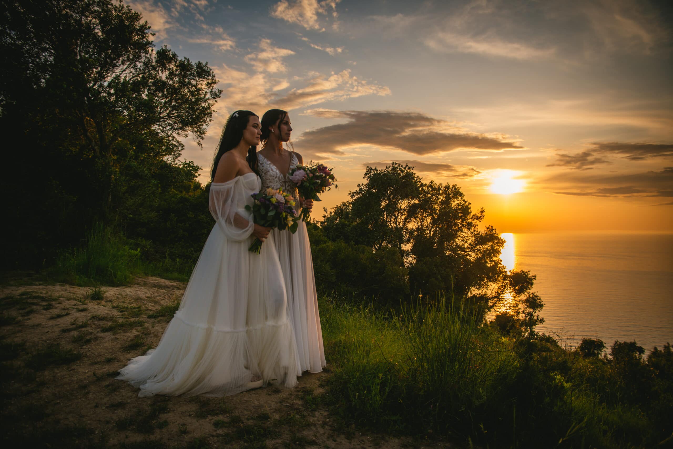 Brides standing tall on a cliff as the sun sets, their love shining in Corfu elopement.