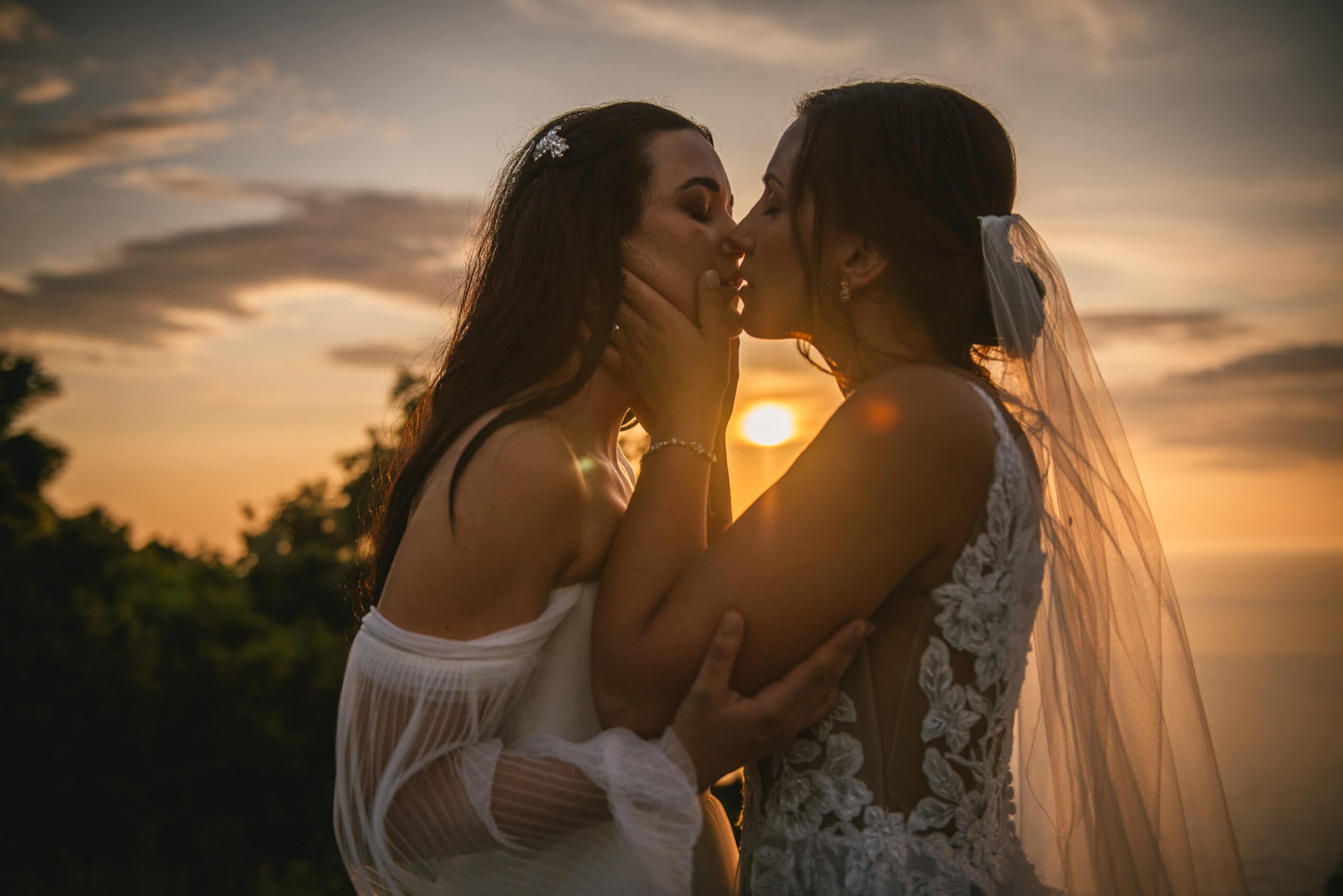 Brides sharing a kiss during sunset's embrace, passion igniting their Corfu elopement.