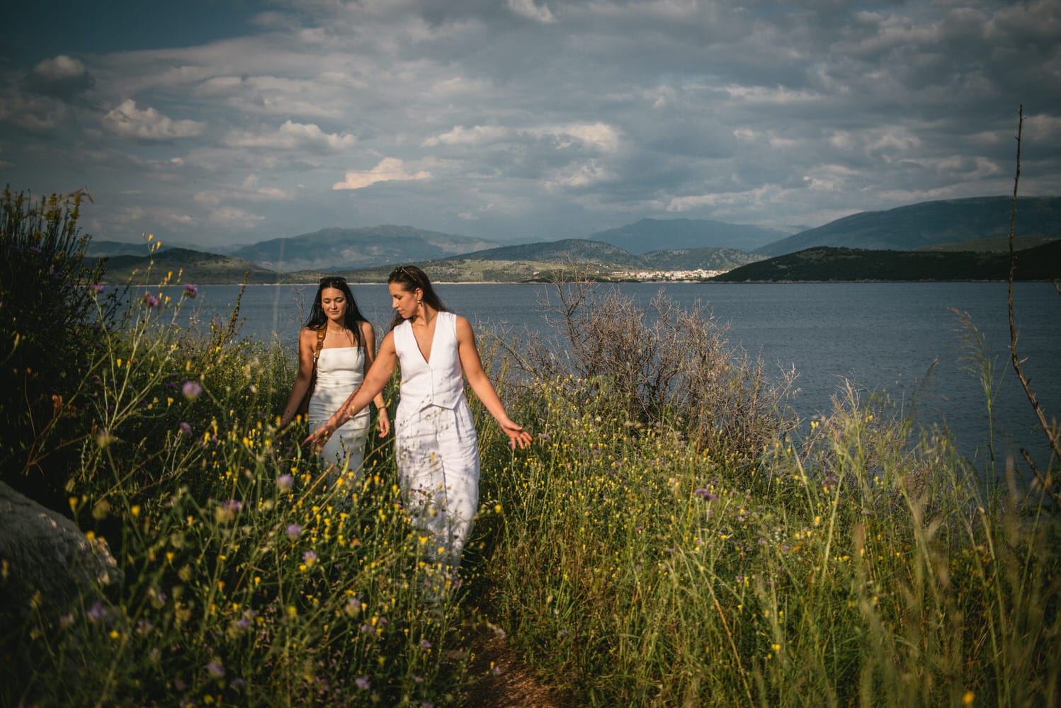 Hand in hand, brides walk along the Corfu coast, love echoing in the waves.