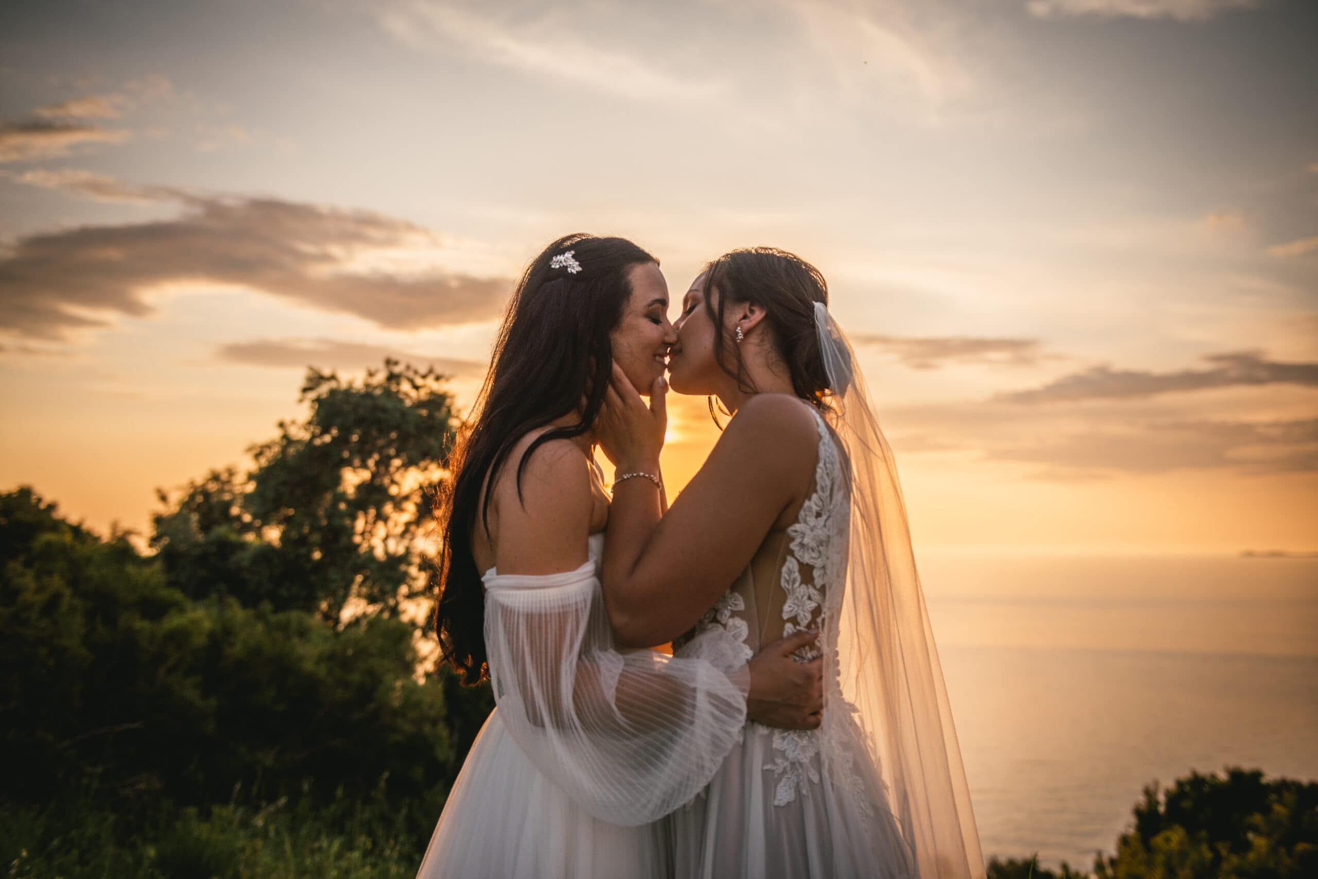 Brides sharing a tender kiss on a cliff, love's height in their Corfu elopement.