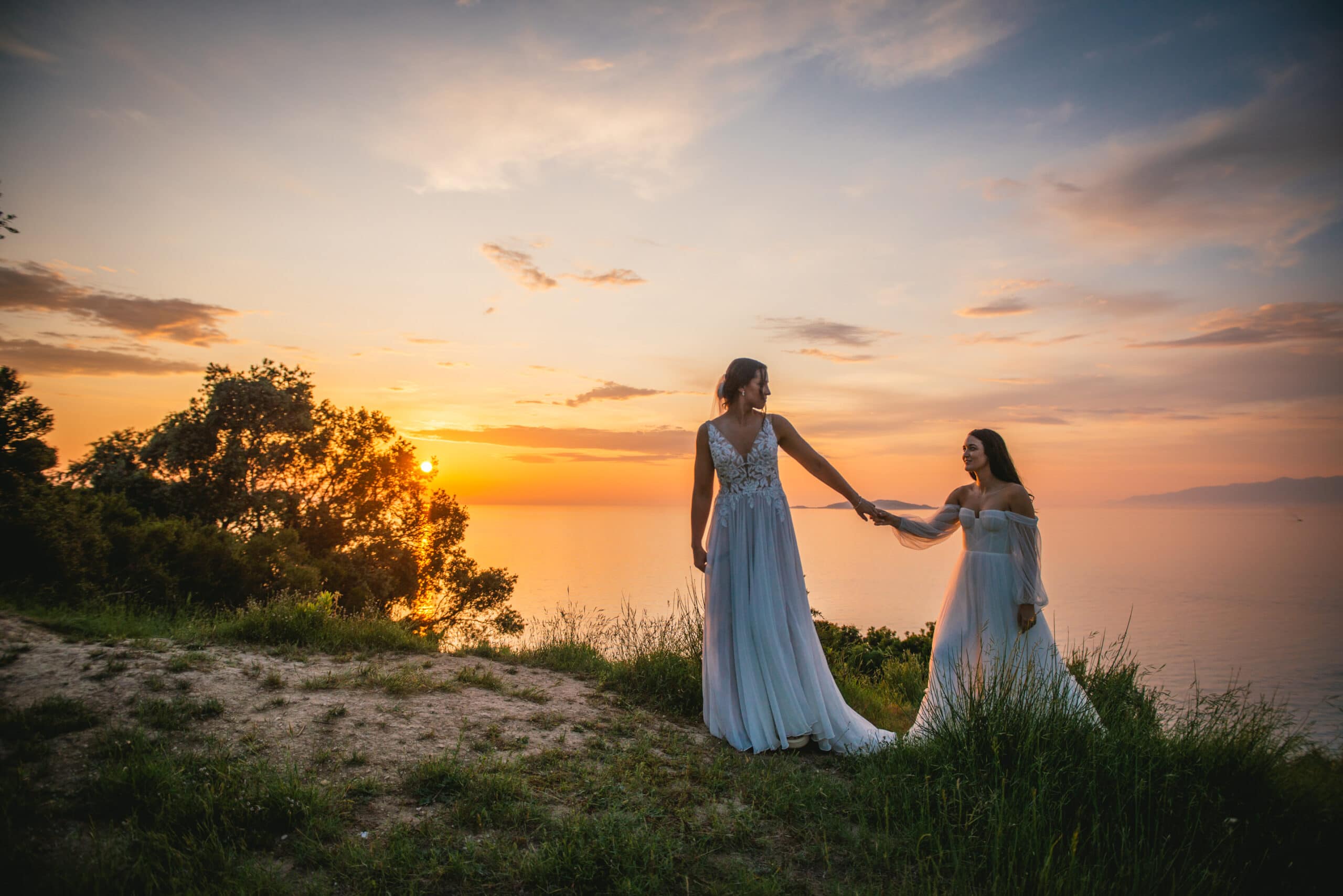 Brides walking along the cliff's edge during sunset, love's journey in Corfu elopement.