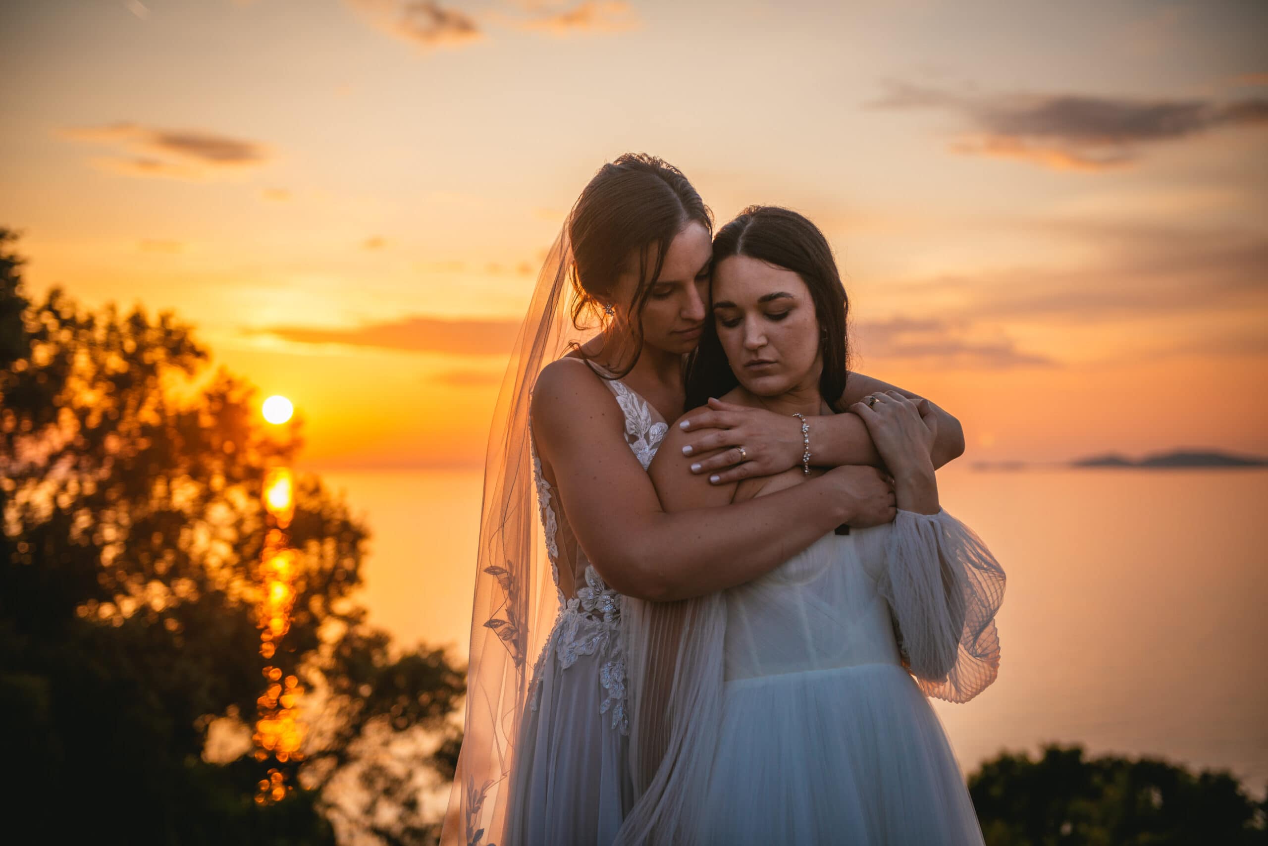 Brides snuggled in each other's arms as the sun sets, a warm moment in Corfu elopement.