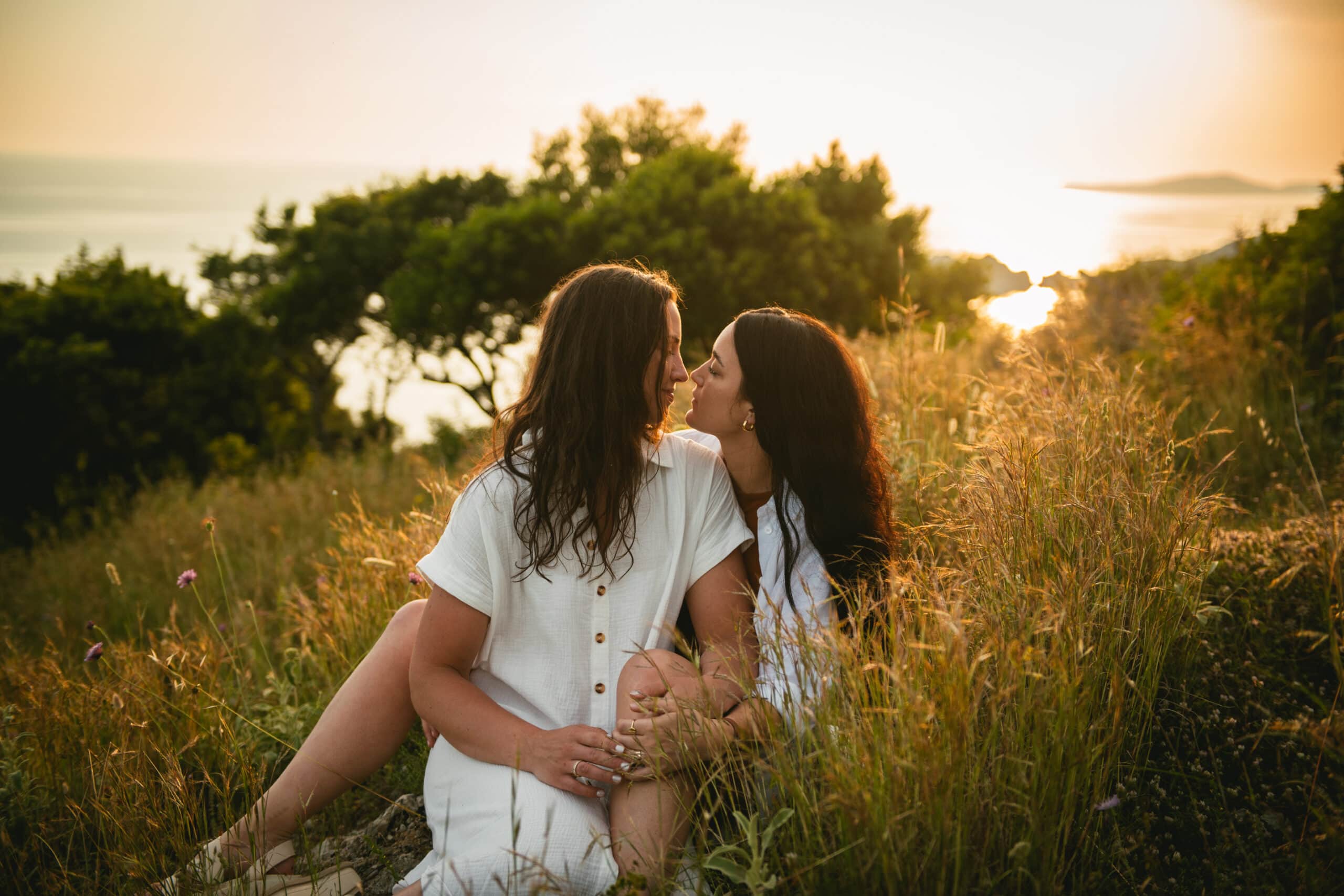 Brides sharing a heartfelt embrace in the soft grass, a touching moment during their Corfu elopement.