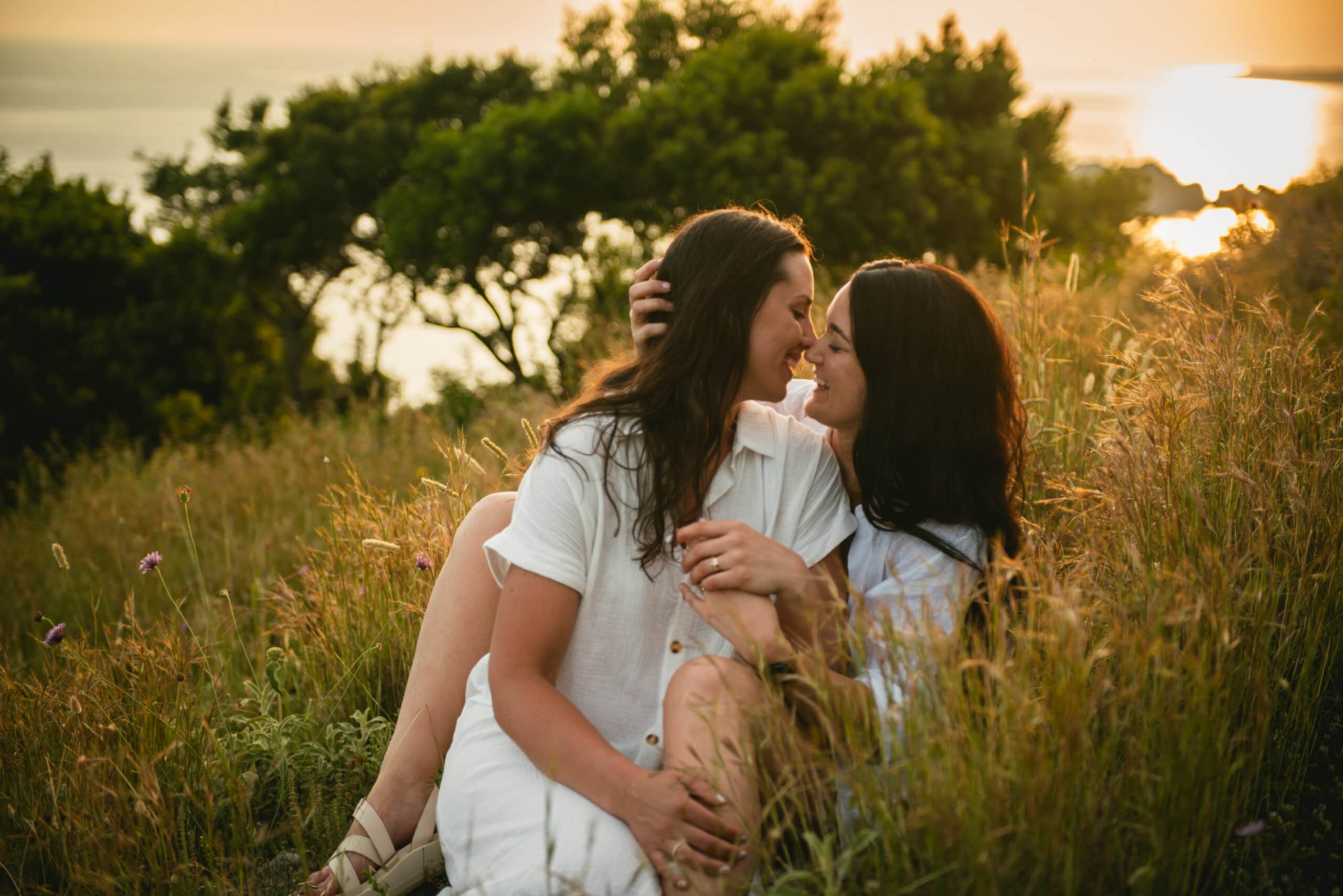 Brides overcome with laughter in the gentle embrace of the grass, adding warmth to their Corfu elopement.