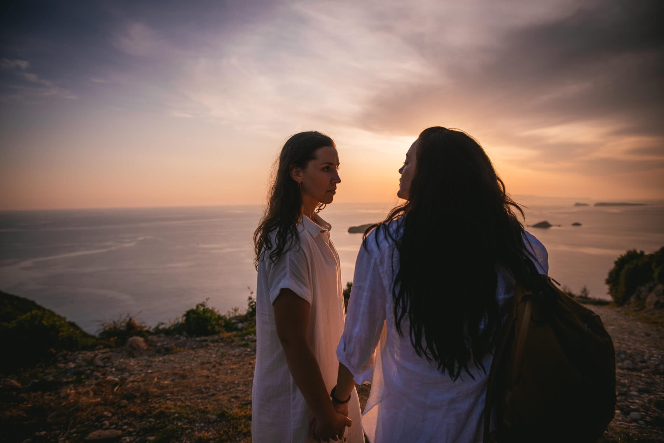 Brides holding hands against the backdrop of a breathtaking Corfu sunset.