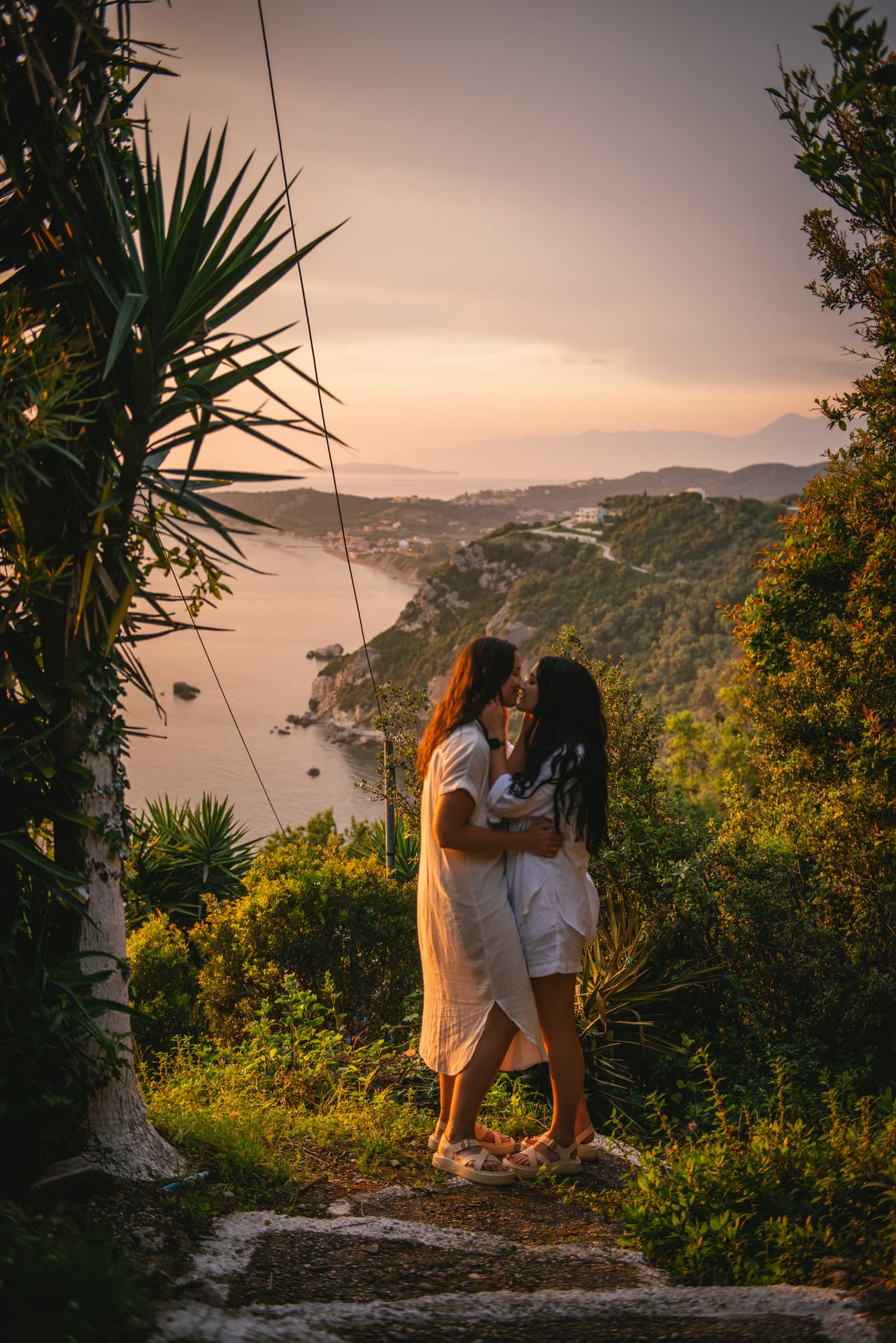 Brides sharing a romantic kiss against the backdrop of a majestic cliff during their Corfu elopement.