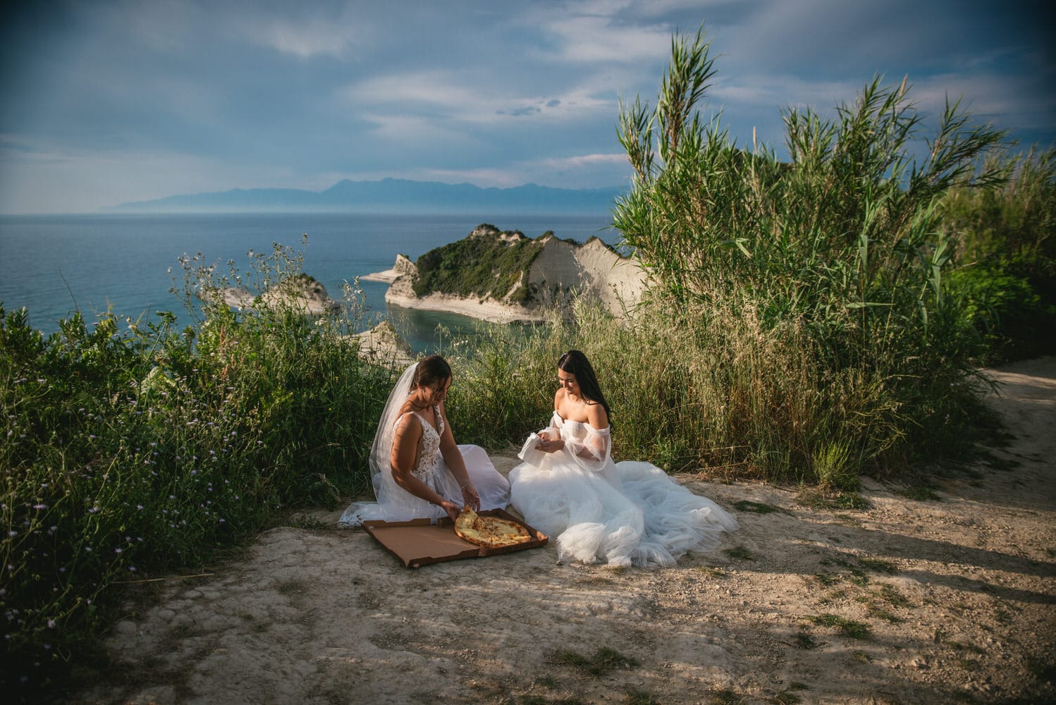 Playful embrace: Brides enjoy pizza at a shop near the cliffs during their Corfu elopement.