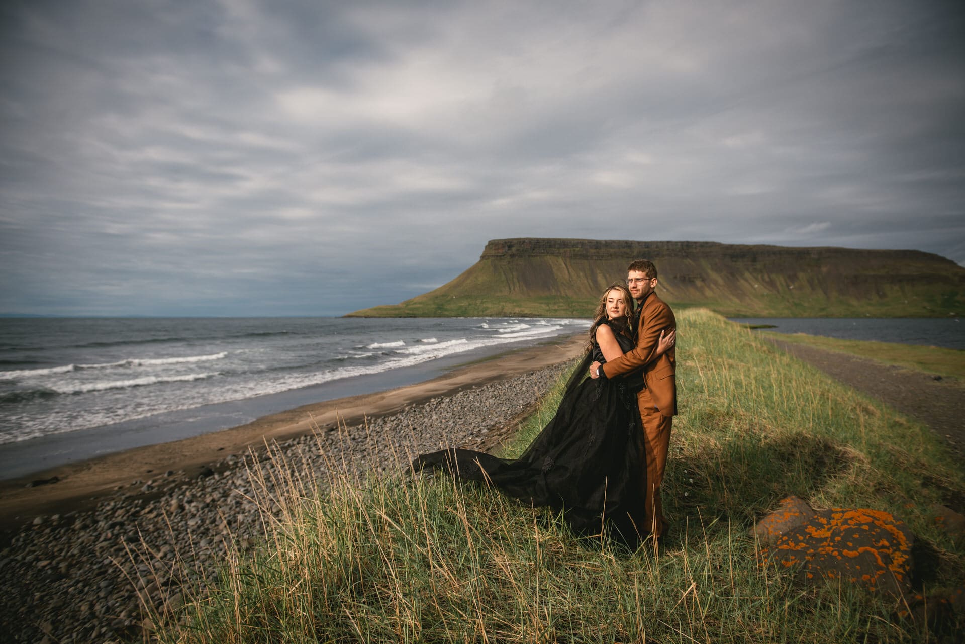 Newlyweds walking hand in hand on a black sand beach as the sun sets over the Westfjords.