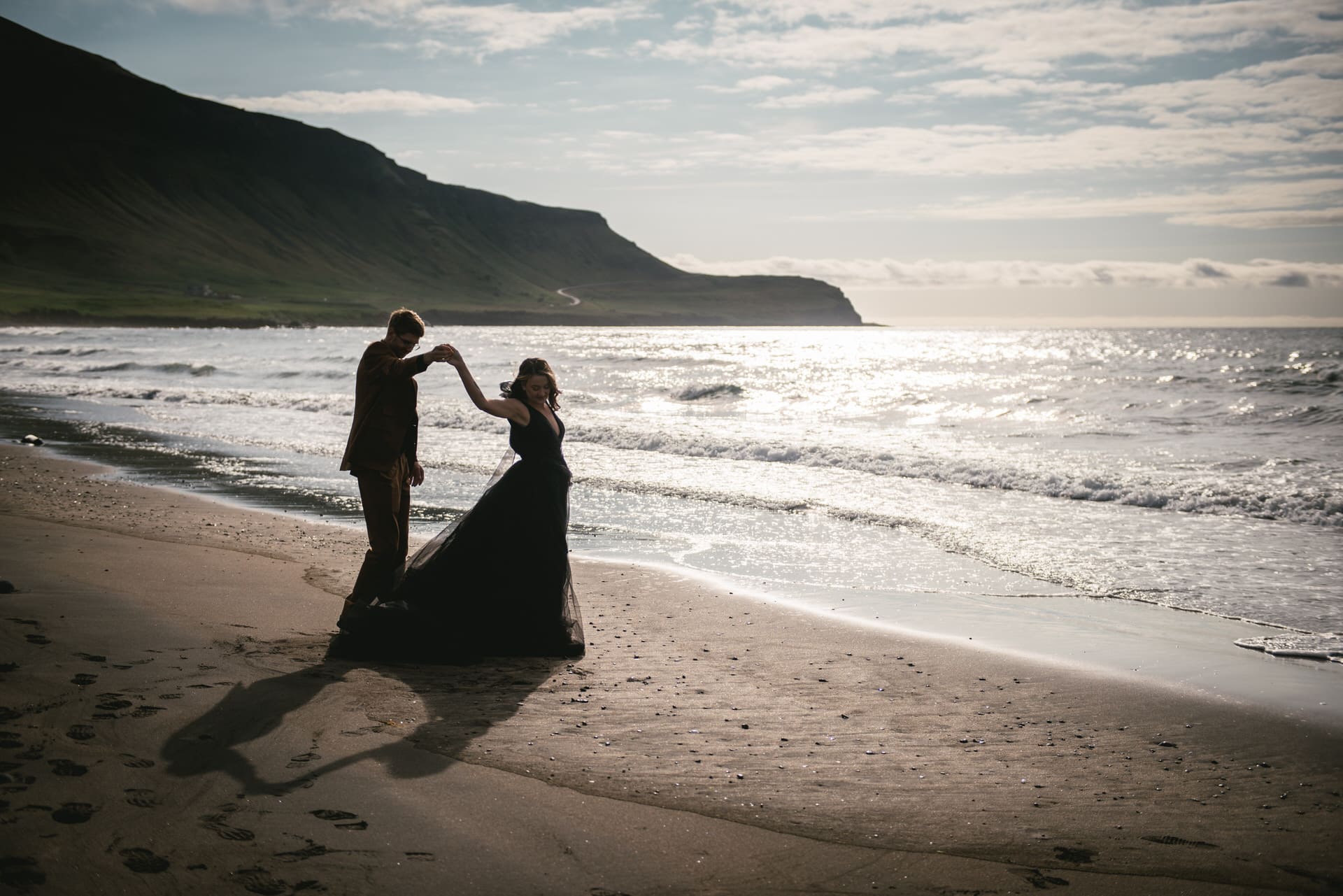 Groom twirls his bride against the backdrop of a tranquil fjord in the Westfjords.