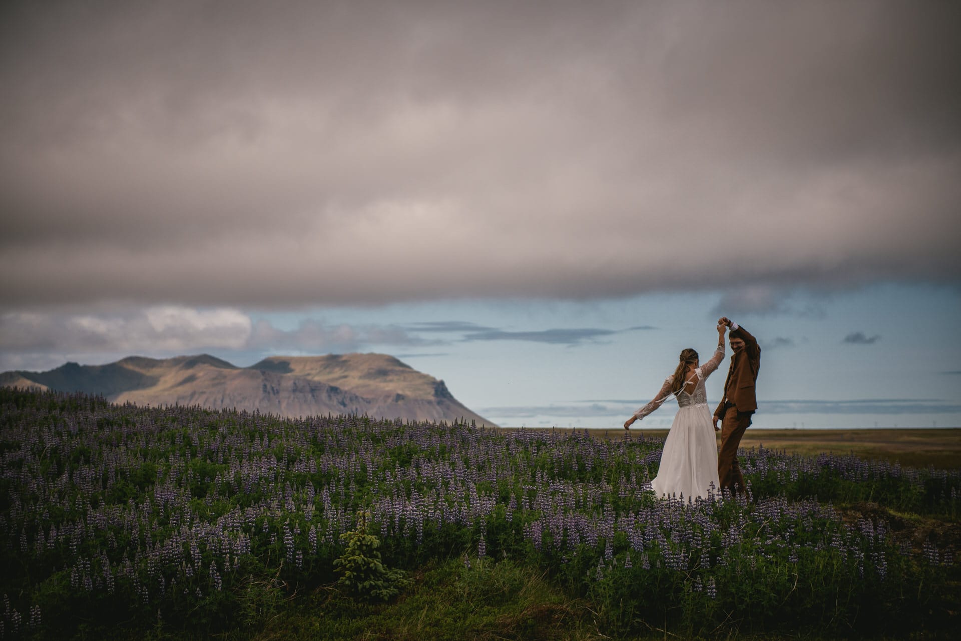 Groom spins his bride amidst a sea of wildflowers during their Westfjords elopement.