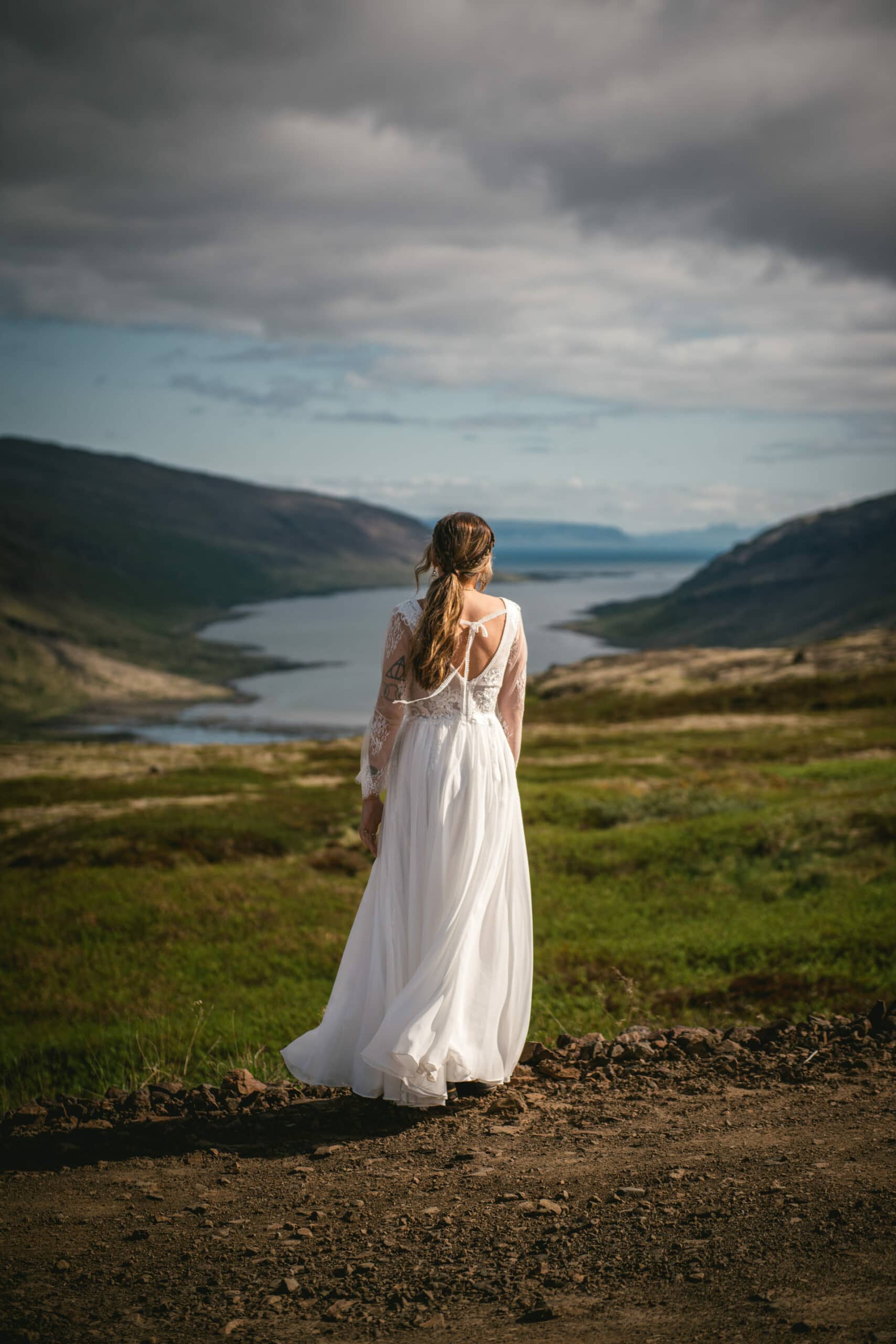 From behind, the bride gazes at the picturesque Westfjords, embodying the anticipation and beauty of her Iceland elopement journey.