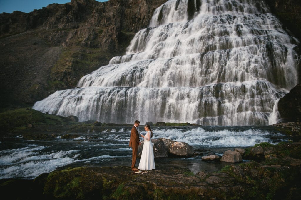 Heartfelt exchange of vows as the couple stands beside a secluded Icelandic waterfall.