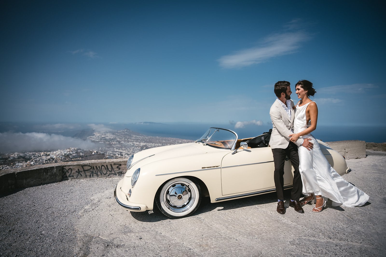 The car, the couple, the crest of Santorini—a tableau of elopement elegance