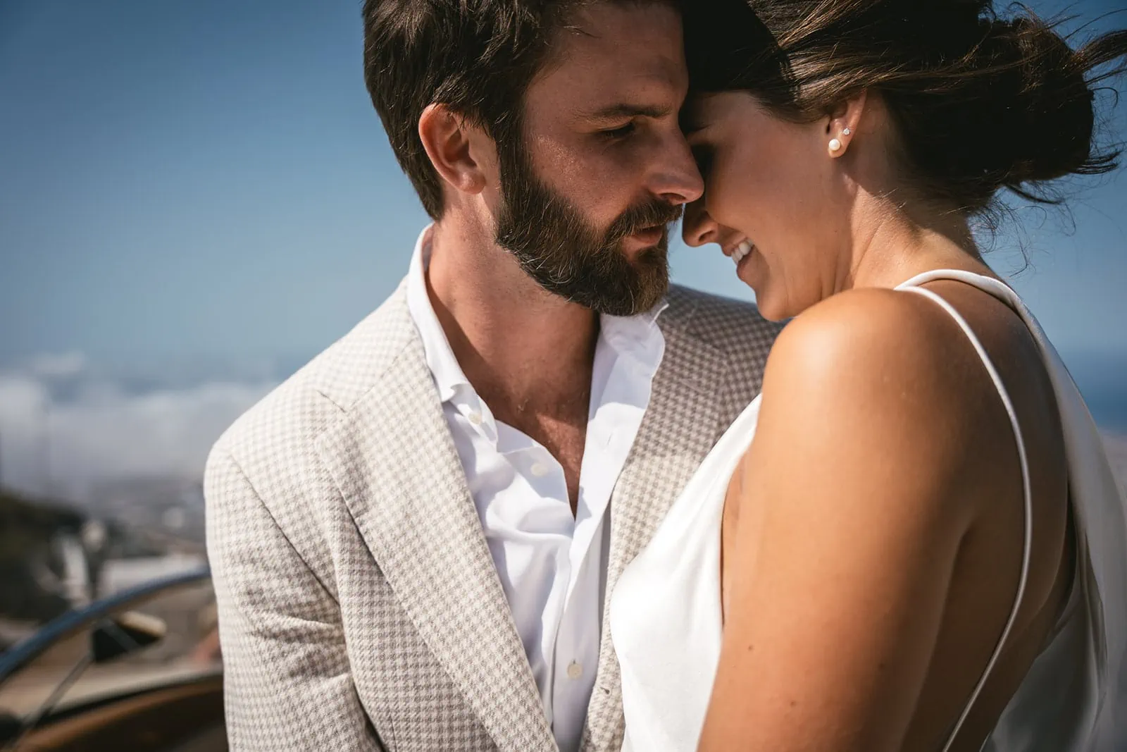 Santorini’s horizon stretches beyond, as they share a moment, vintage style, above the world