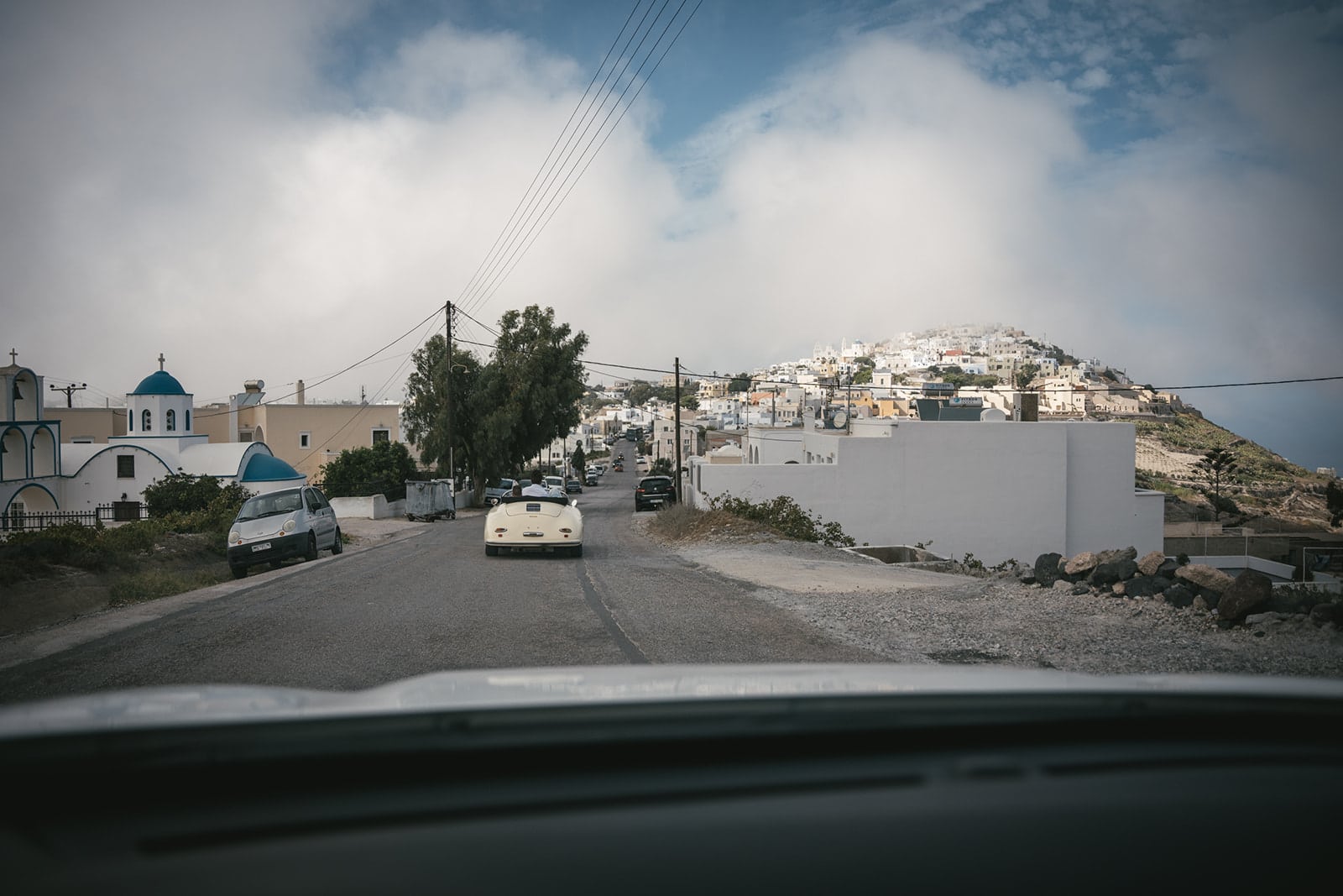 Santorini's blue backdrop frames a moment of timeless romance by the vintage car