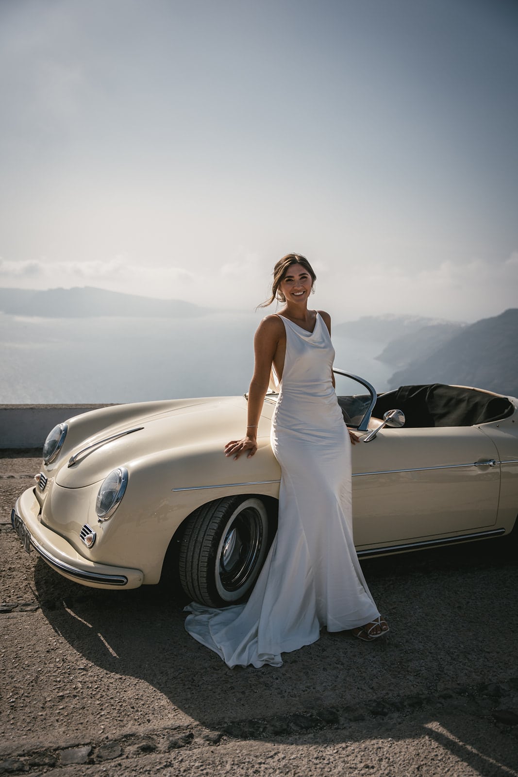 The sea’s expanse witnesses their promise of adventure, framed by the vintage car’s elegance