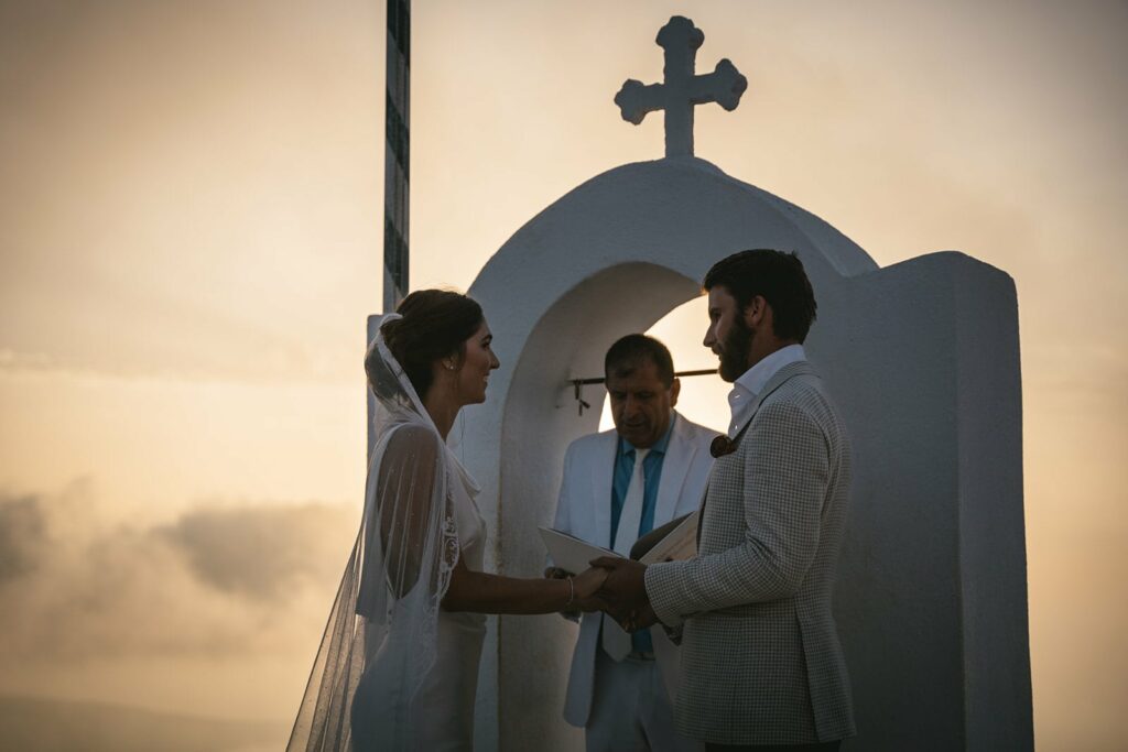 The glow of sunset envelops them, their promises shining as bright as the Santorini sky