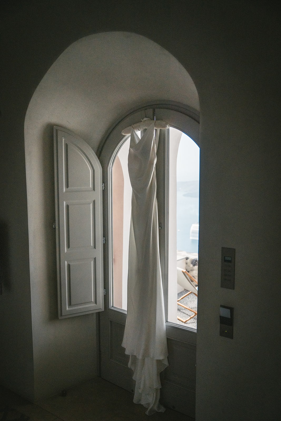 Wedding dress hanging by the window, bathed in Santorini light, ready for its debut