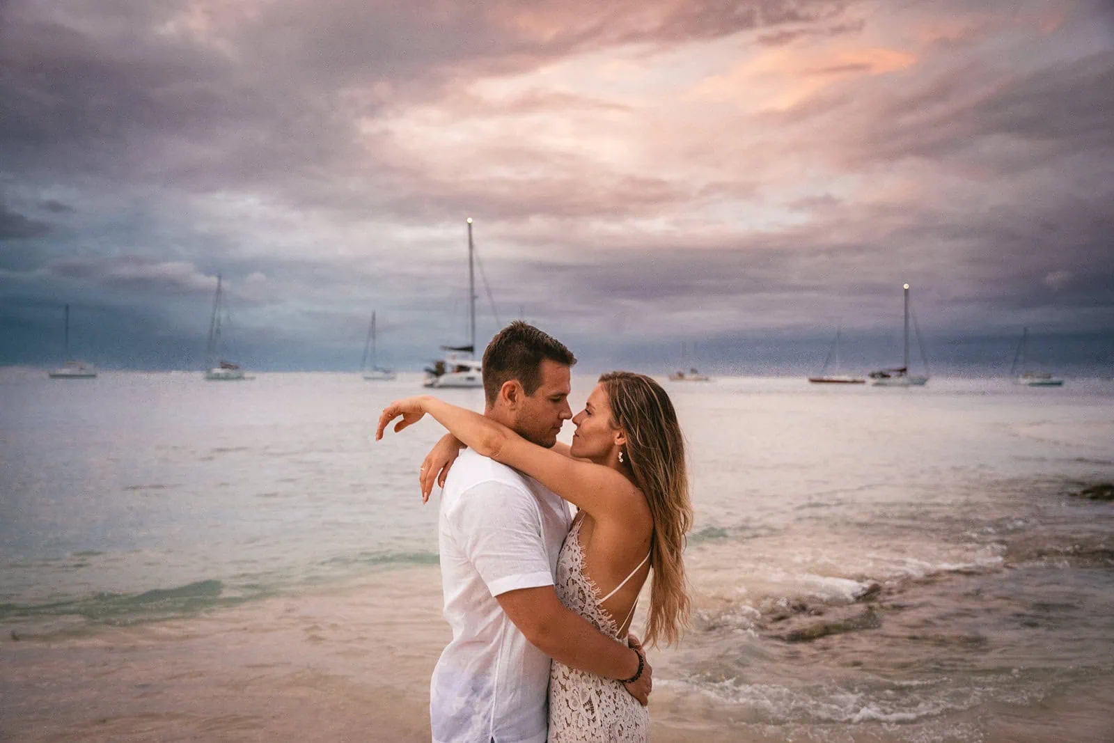 Bride and groom embracing under a palm tree, framed by a beautiful French Polynesia sunset