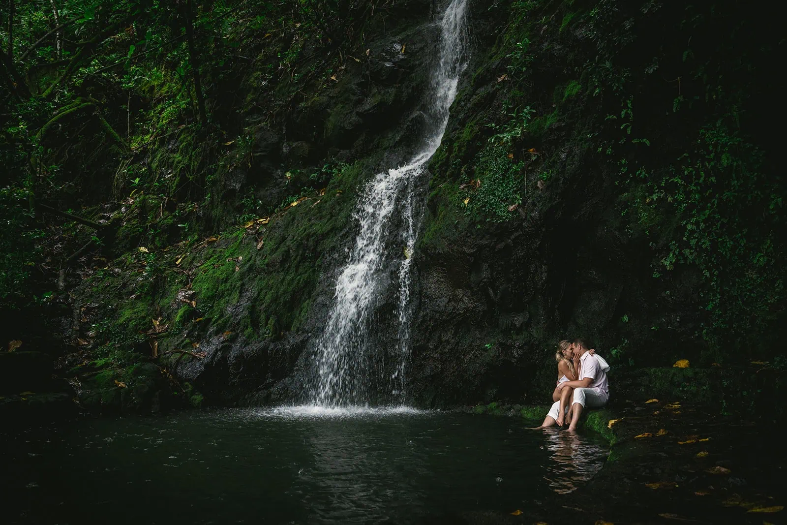 Bride and groom sitting under a waterfall, their feet dangling over the waters of French Polynesia.