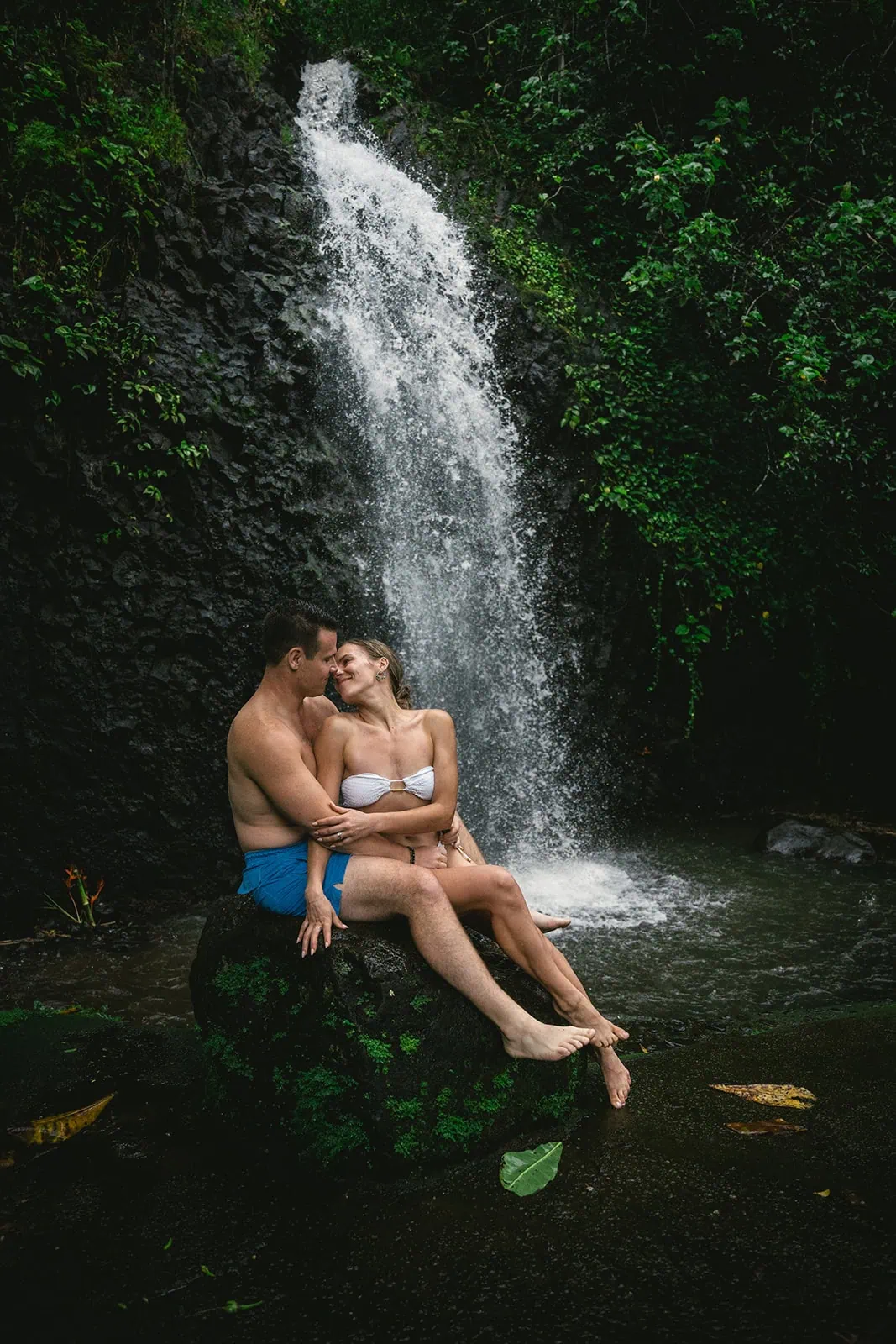 Bride and groom kissing near a waterfall in French Polynesia.