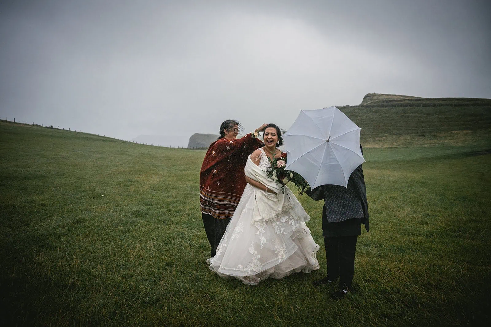 The bride smiling under a veil of raindrops at Dunluce Castle elopement